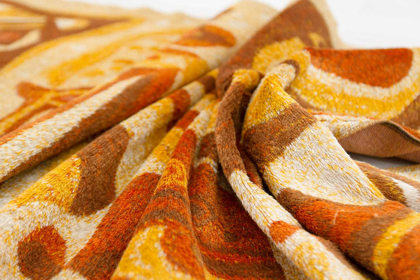 macro shot of an artistically draped vintage tapestry, showcasing the organic abstract design in orange, brown and beige colors and the fine pile structure of the mid century tapestry fabric