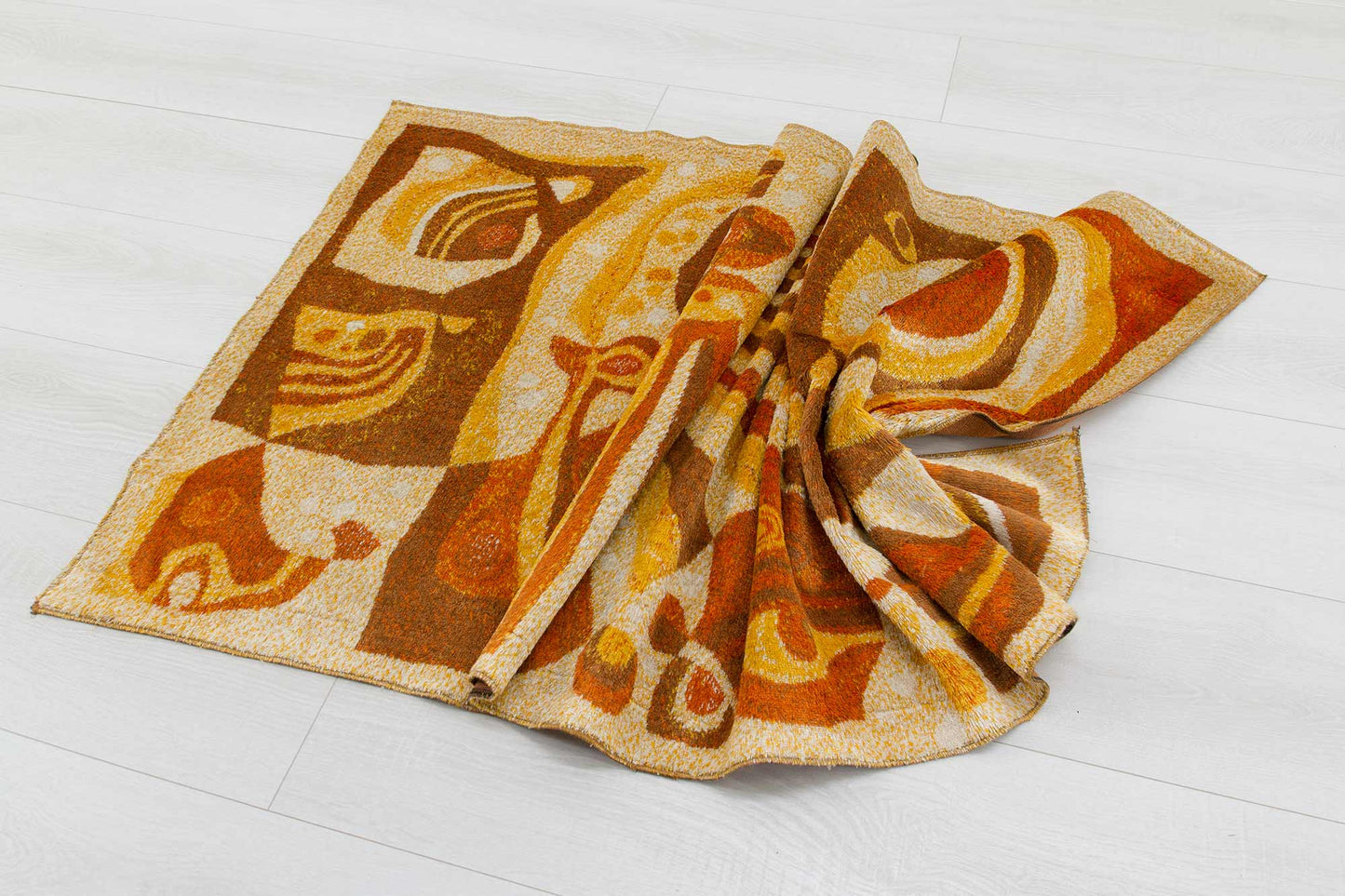 Slightly angled top view of an artistically draped vintage tapestry, showcasing the organic abstract design in orange, brown and beige colors of the mid century tapestry fabric