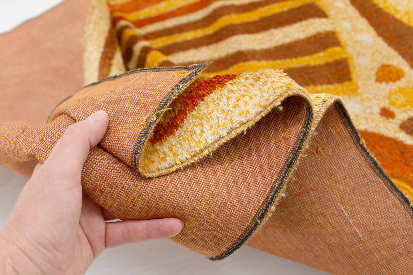 1960s mid century modern tapestry fabric held in hand, showing the soft pile structure and both sides of the woven fabric, the warm colors and organic abstract pattern