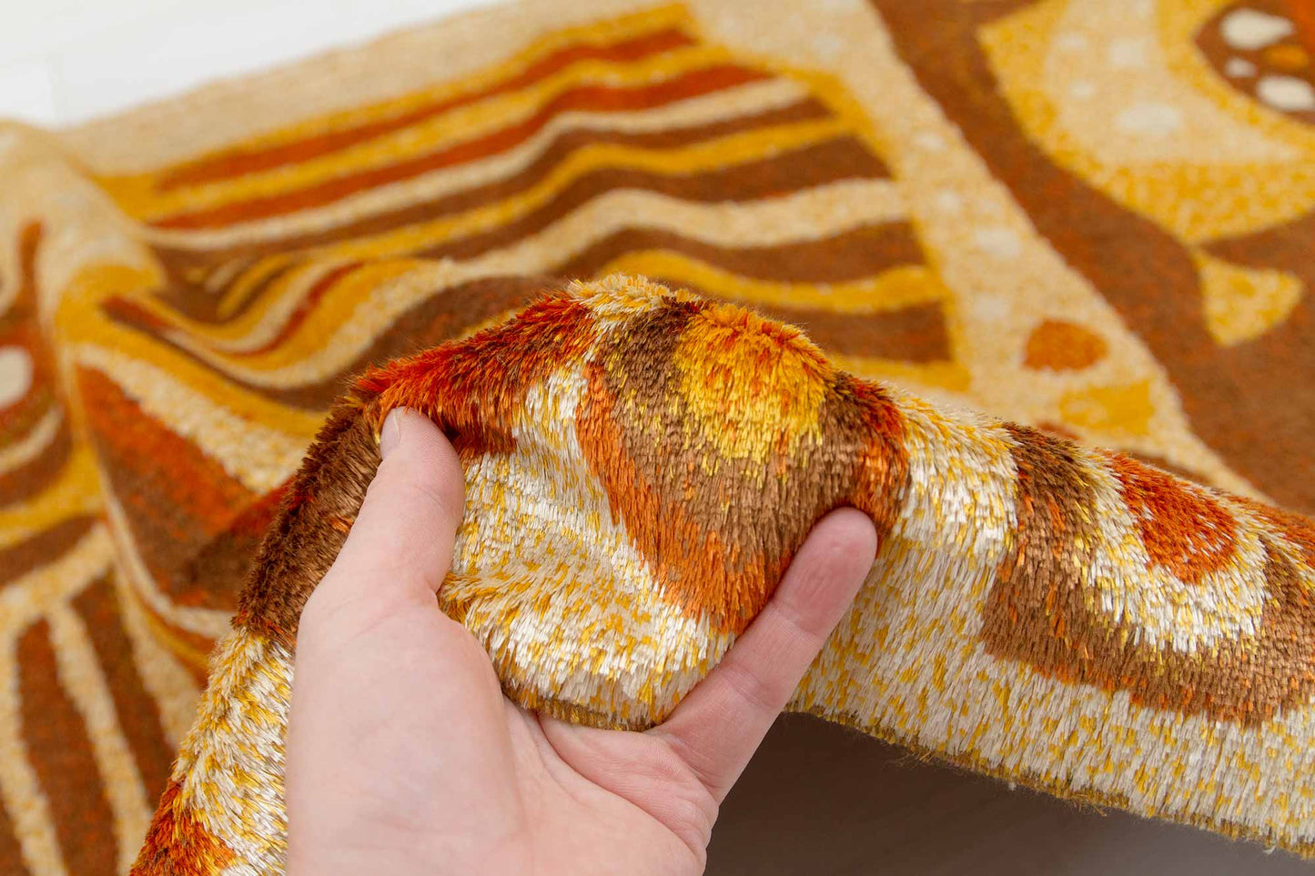 mid century modern tapestry fabric held in hand, demonstrating the soft pile structure of the woven tapestry fabric, the warm colors and organic abstract pattern