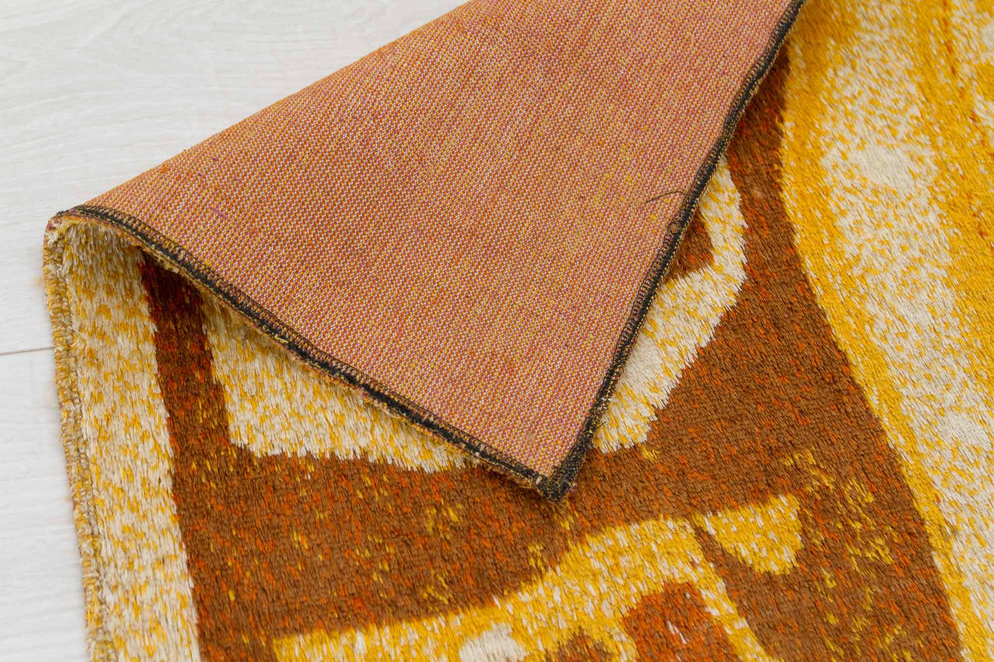 corner of a 1960s vintage mid century modern wall tapestry folded over, showcasing the fine piles of the tapestry fabric, the typical mid-century color scheme and the woven underside of the fabric