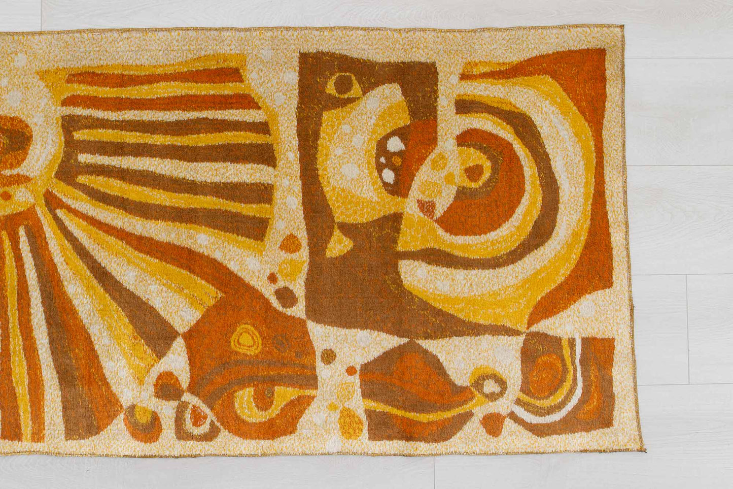 closeup of a vintage mid century modern wall tapestry, laid flat on a white floor, showing the busy abstract-organic patterns of the soft fabric and its warm beige, orange and brown color combination