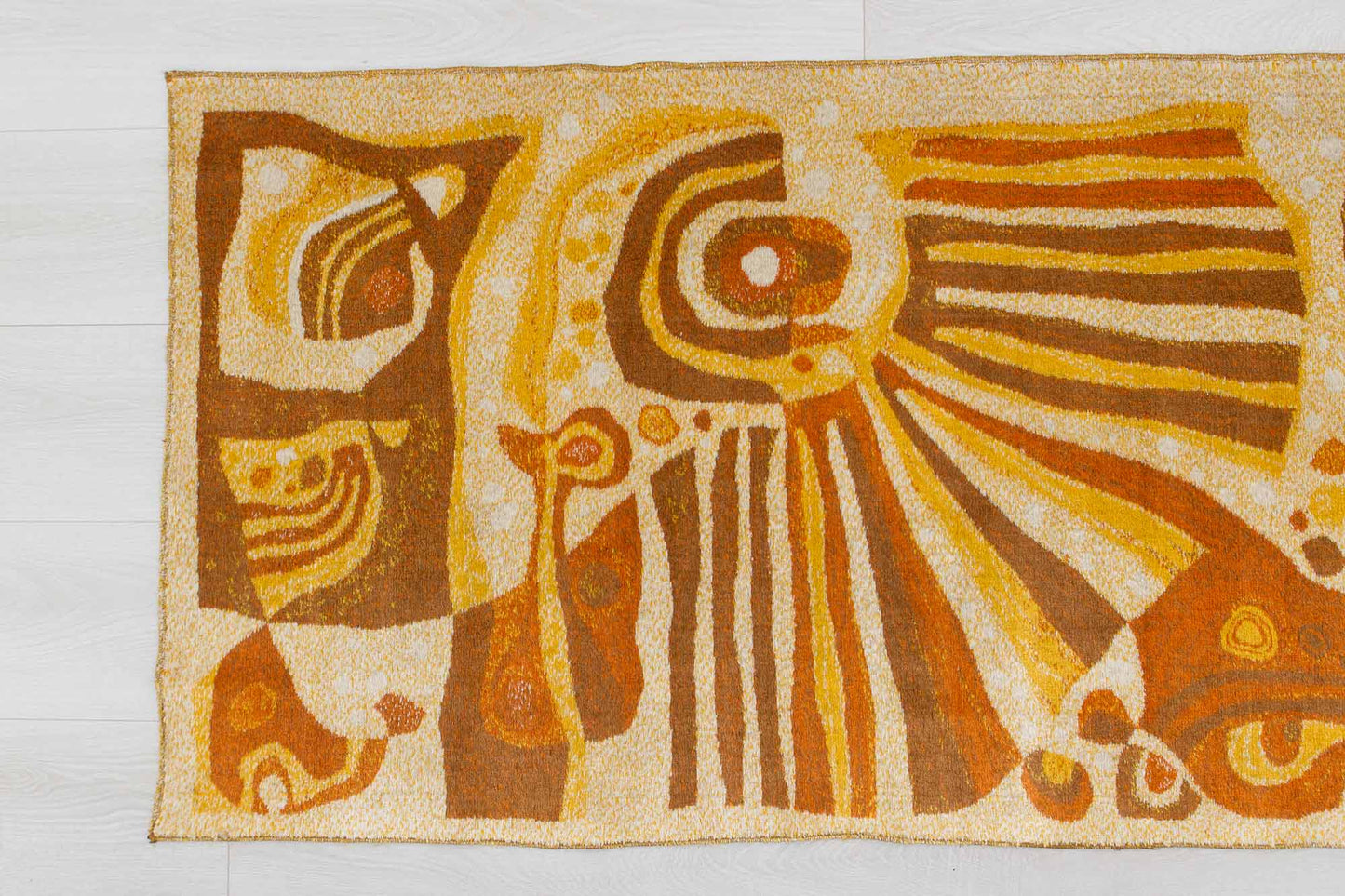 closeup of a vintage mid century modern wall tapestry, laid flat on a white floor, showing the busy abstract-organic patterns of the soft fabric and its warm beige, brown and orange color combination