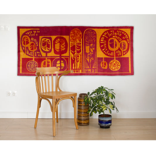 Large vintage 1960s tapestry in fiery red, burgundy and orange tones, styled as Mid-Century Modern wall decor above a Thonet chair and plant in a living room setting