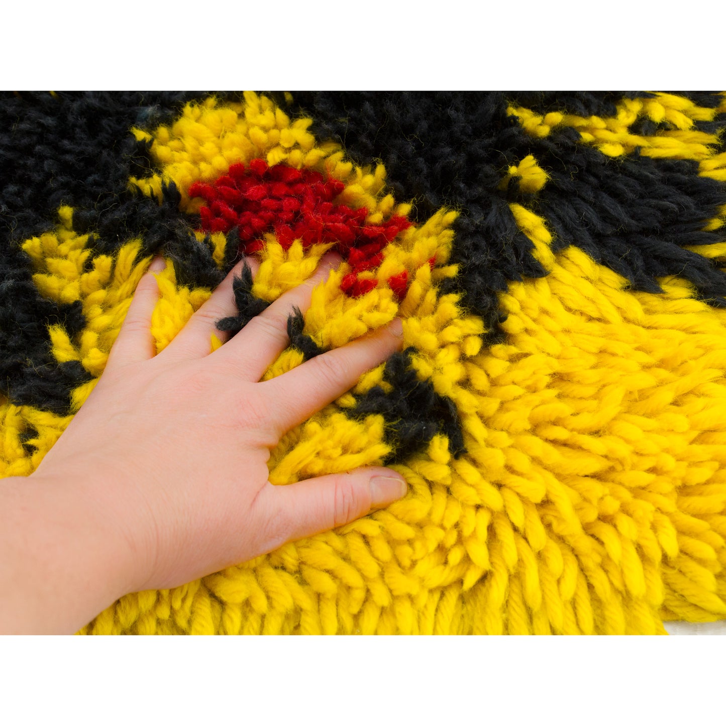 A hand pressing deep into the soft, thick piles of the canary yellow vintage rya rug, demonstrating the extra high pile depth and rich, cozy tactile quality.