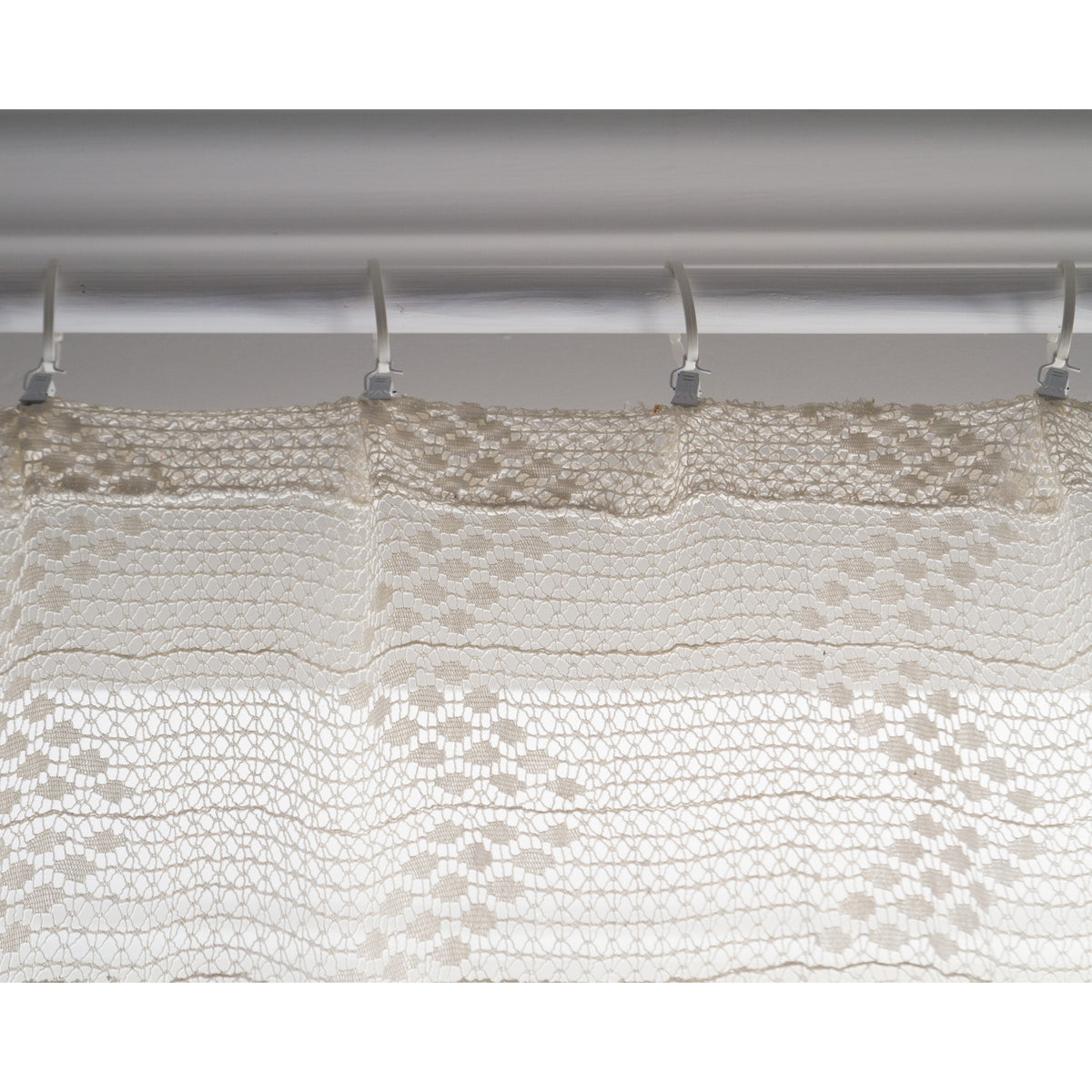 Top edge of vintage lace curtain hung with curtain clips on a white rod