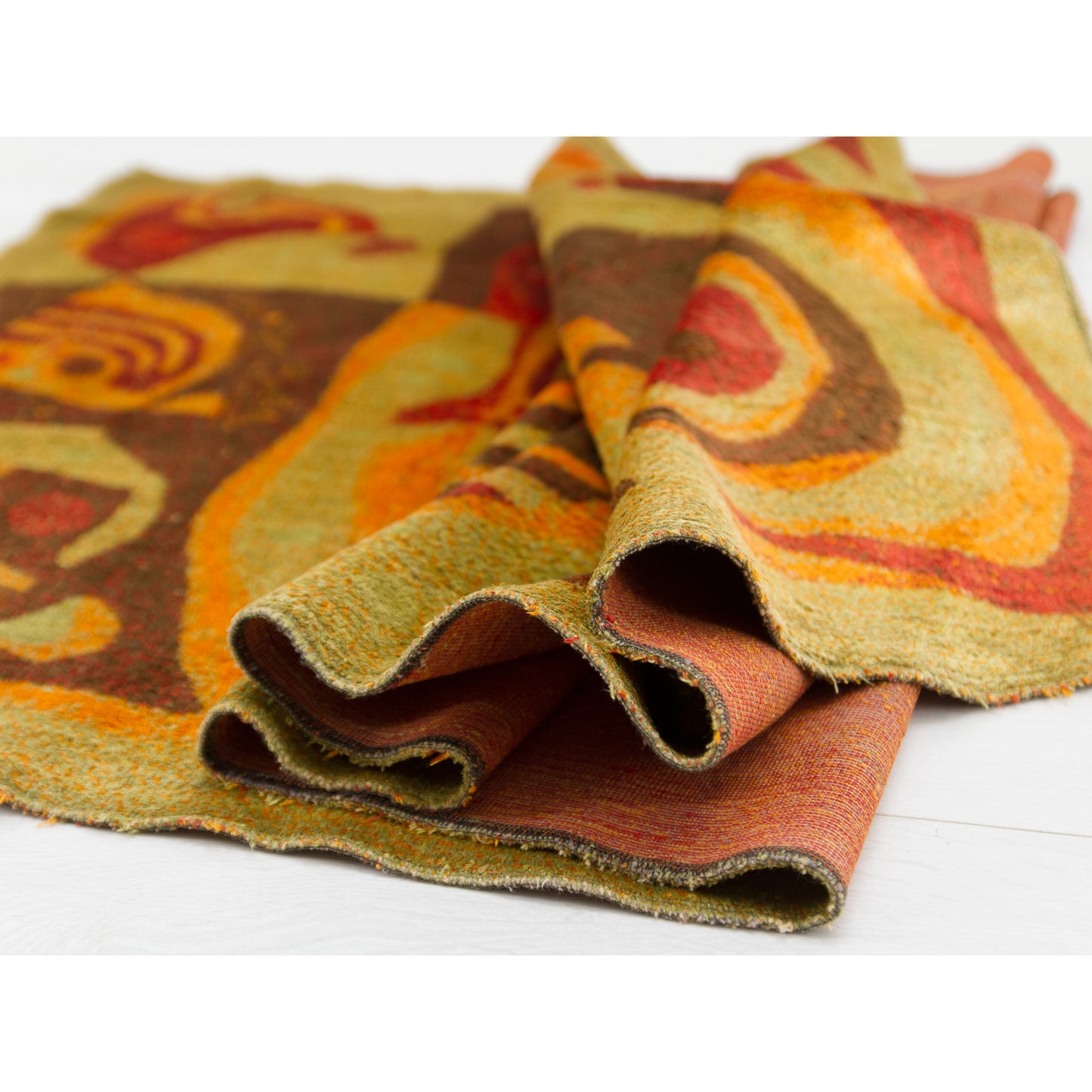 The Emese tapestry artfully rolled to show its weight and sculptural potential. Highlights the vibrant interaction between the russet red, orange, and olive green plush surfaces.
