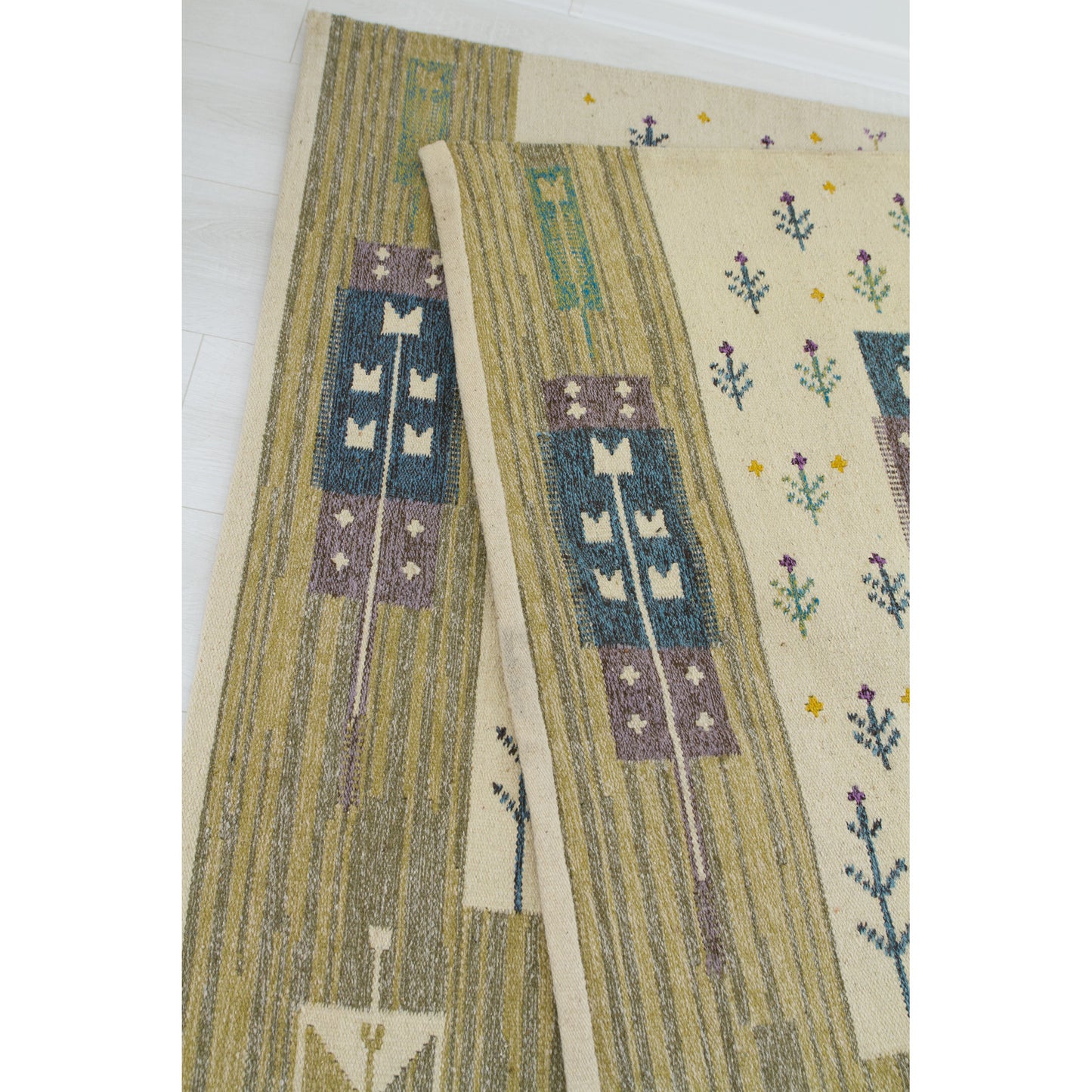 Close up focusing on the neatly finished and cleanly hemmed edge of the mid-century handwoven flatweave rug.