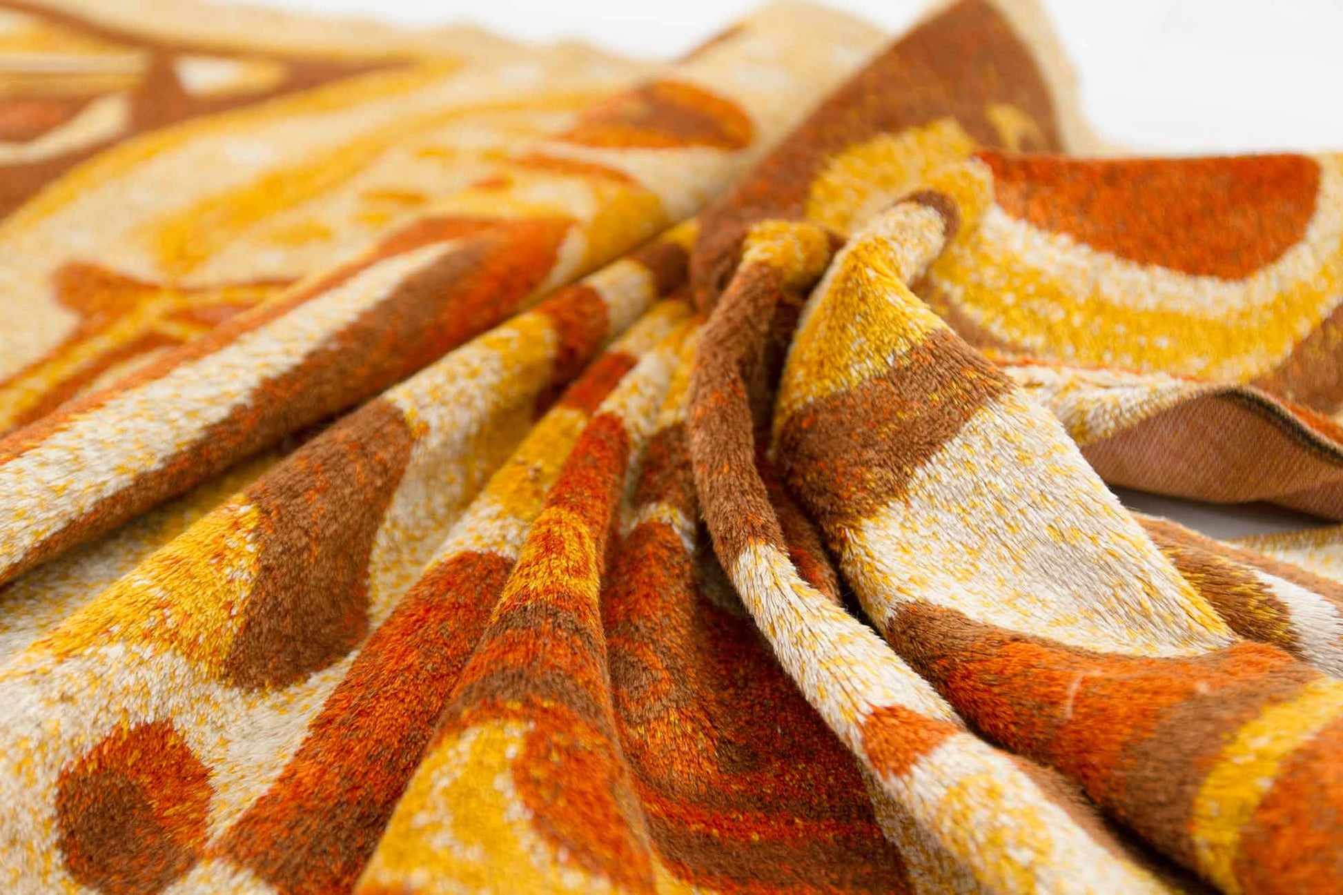 macro shot of an artistically draped vintage tapestry, showcasing the organic abstract design in orange, brown and beige colors and the fine pile structure of the mid century tapestry fabric