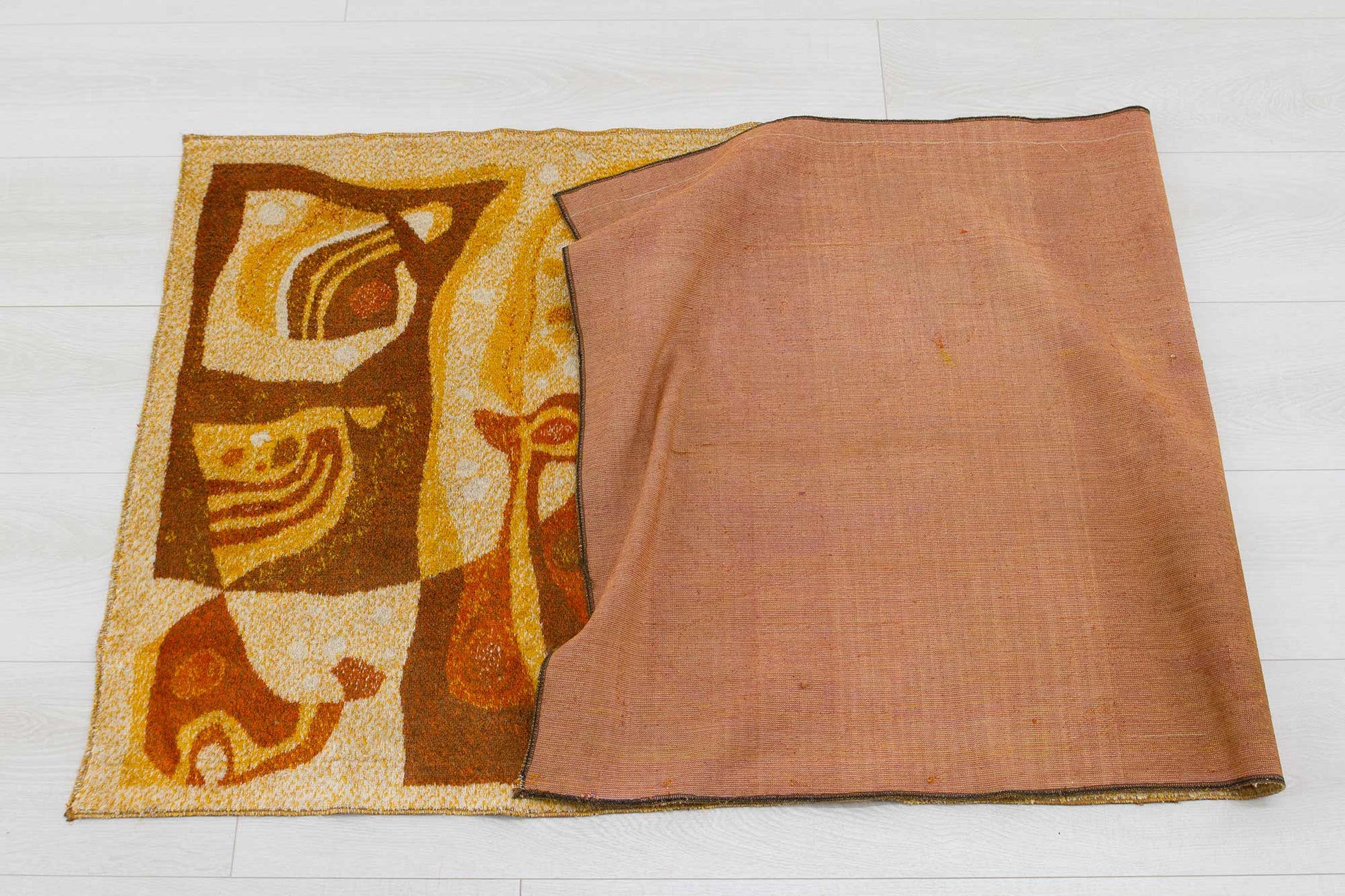 1960s vintage mid century modern wall tapestry halfway folded over, showcasing the organic abstract design in orange, brown and beige colors and the woven underside of the vintage fabric