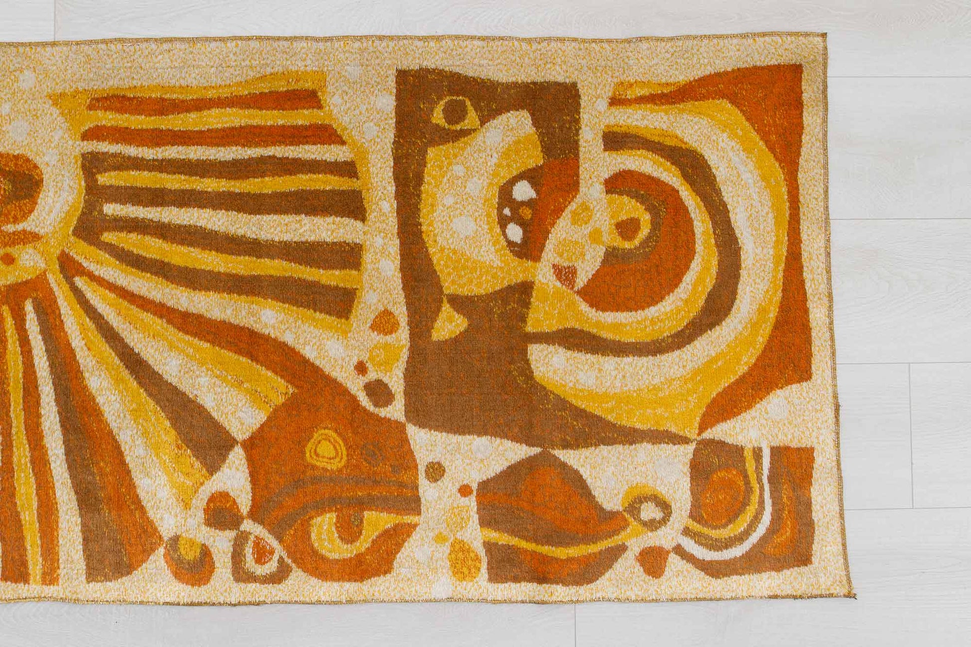 closeup of a vintage mid century modern wall tapestry, laid flat on a white floor, showing the busy abstract-organic patterns of the soft fabric and its warm beige, orange and brown color combination