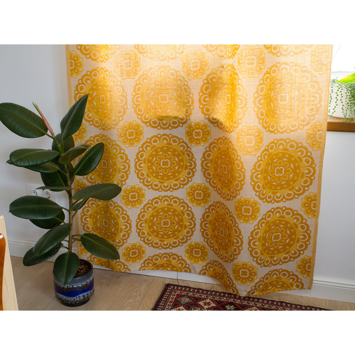 Full length 1970s yellow curtain panel next to window with green plant for an authentic mid century style.