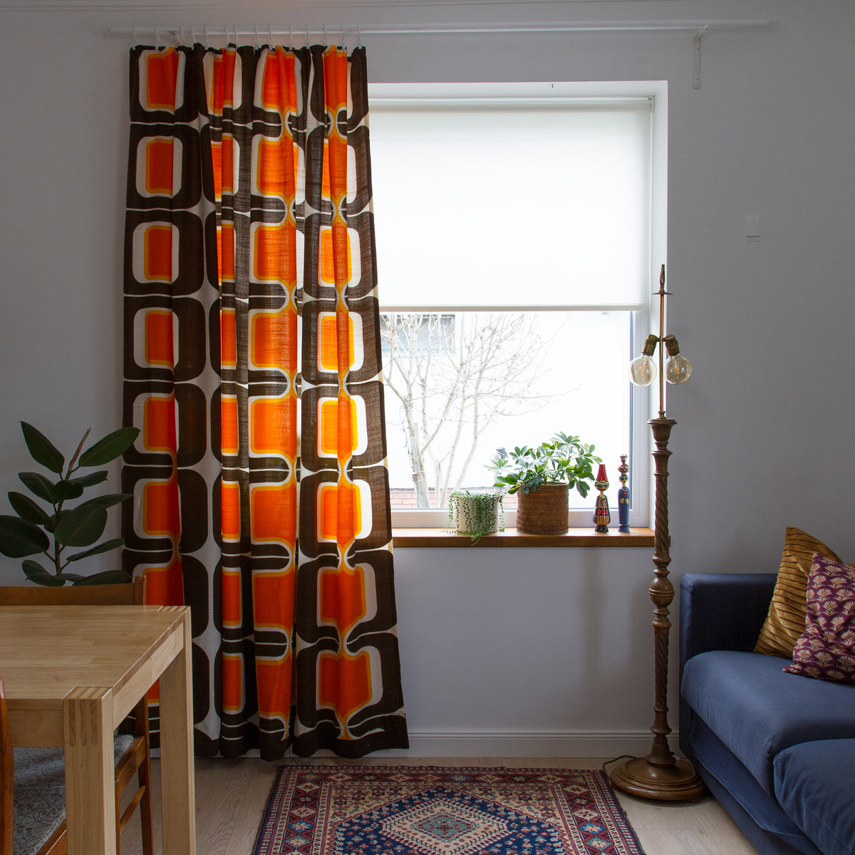 Mid century modern curtain panel on white rod next to a window, glowing 70s orange and chocolate brown retro print.