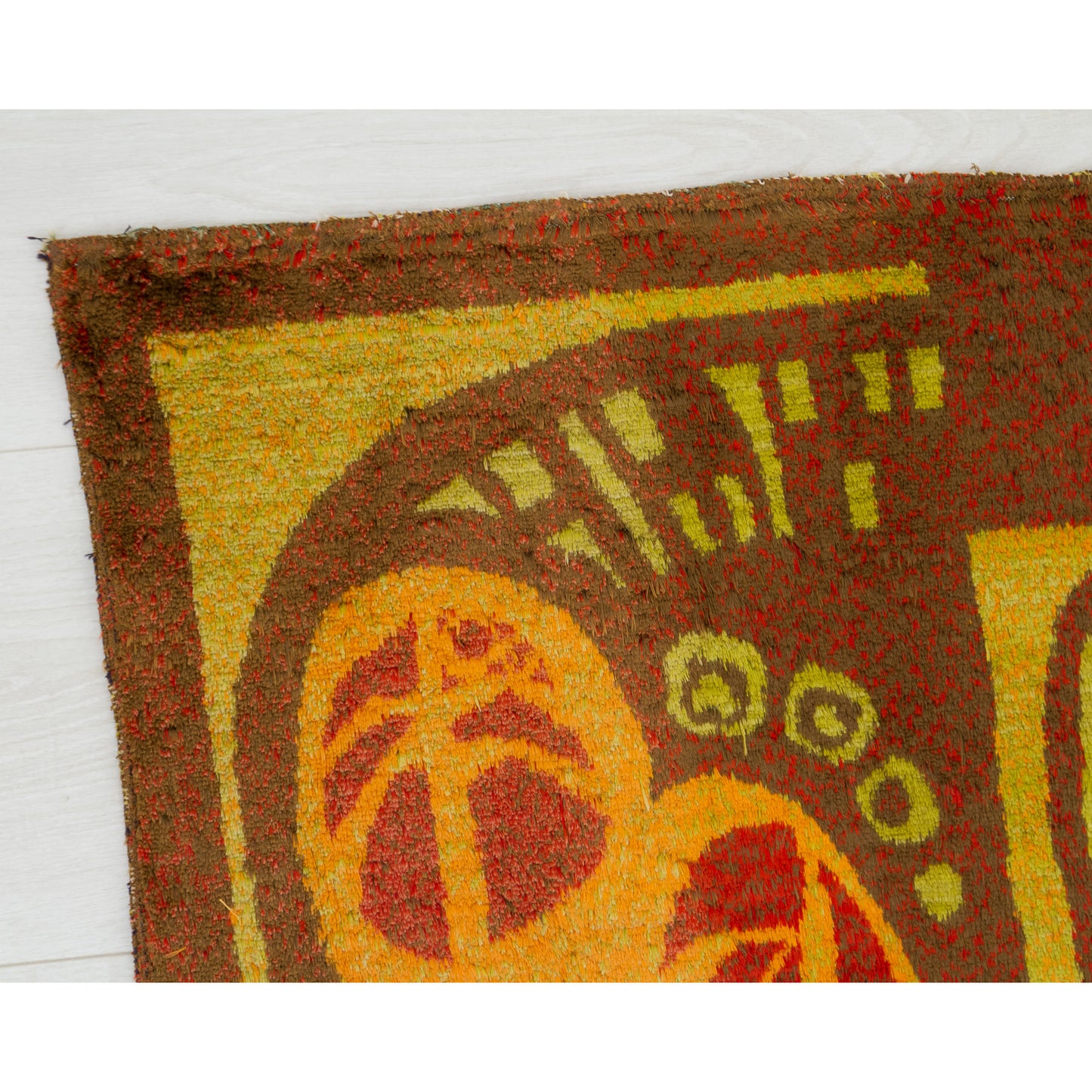 Macro shot of the top left tapestry corner featuring a sun-like organic circle with radiating inner lines over a warm beige background.