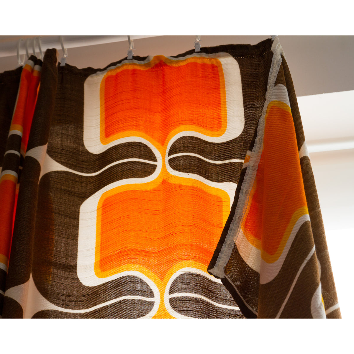 Top of a 60s retro curtain panel with pleat tape sewn on, hanging from white curtain hooks.