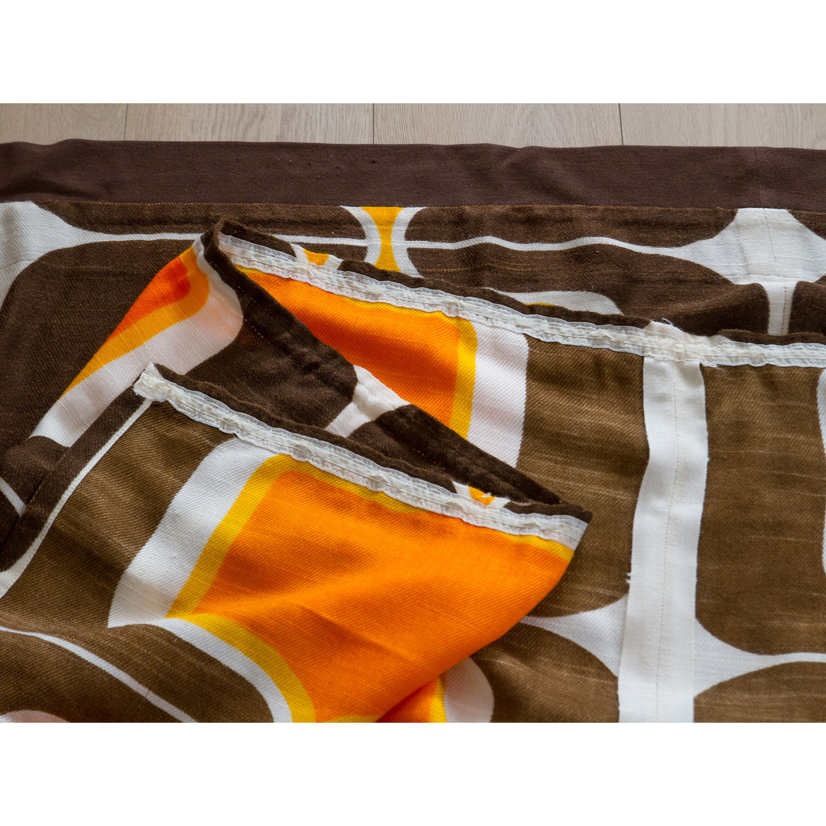 Folded vintage space age curtain textile showing orange, brown and white print and the reverse side, along with pencil pleat tape on top.