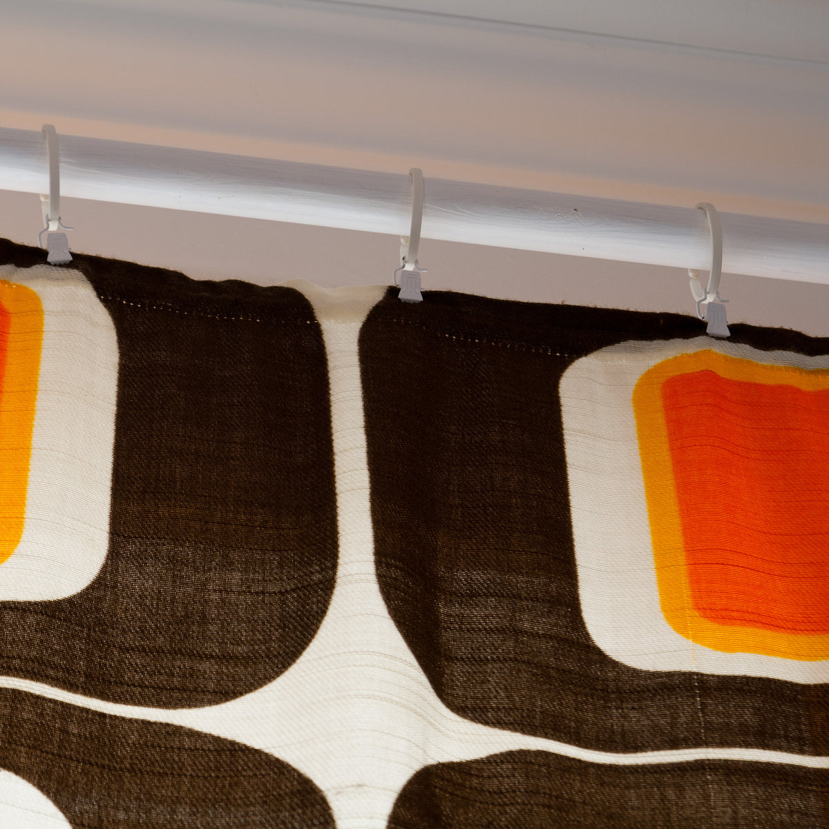 Top of a 1960s vintage curtain panel with pleat tape sewn on, hanging from white curtain hooks with clips