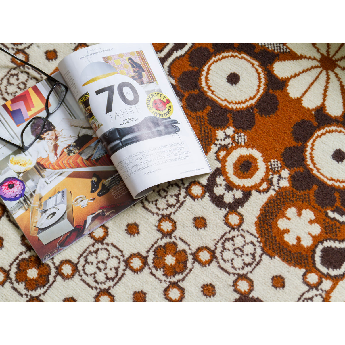 Vintage 70s magazine lying on a flower power rug with brown and ivory flowers, to visually mediate a sense of scale of the bold floral pattern