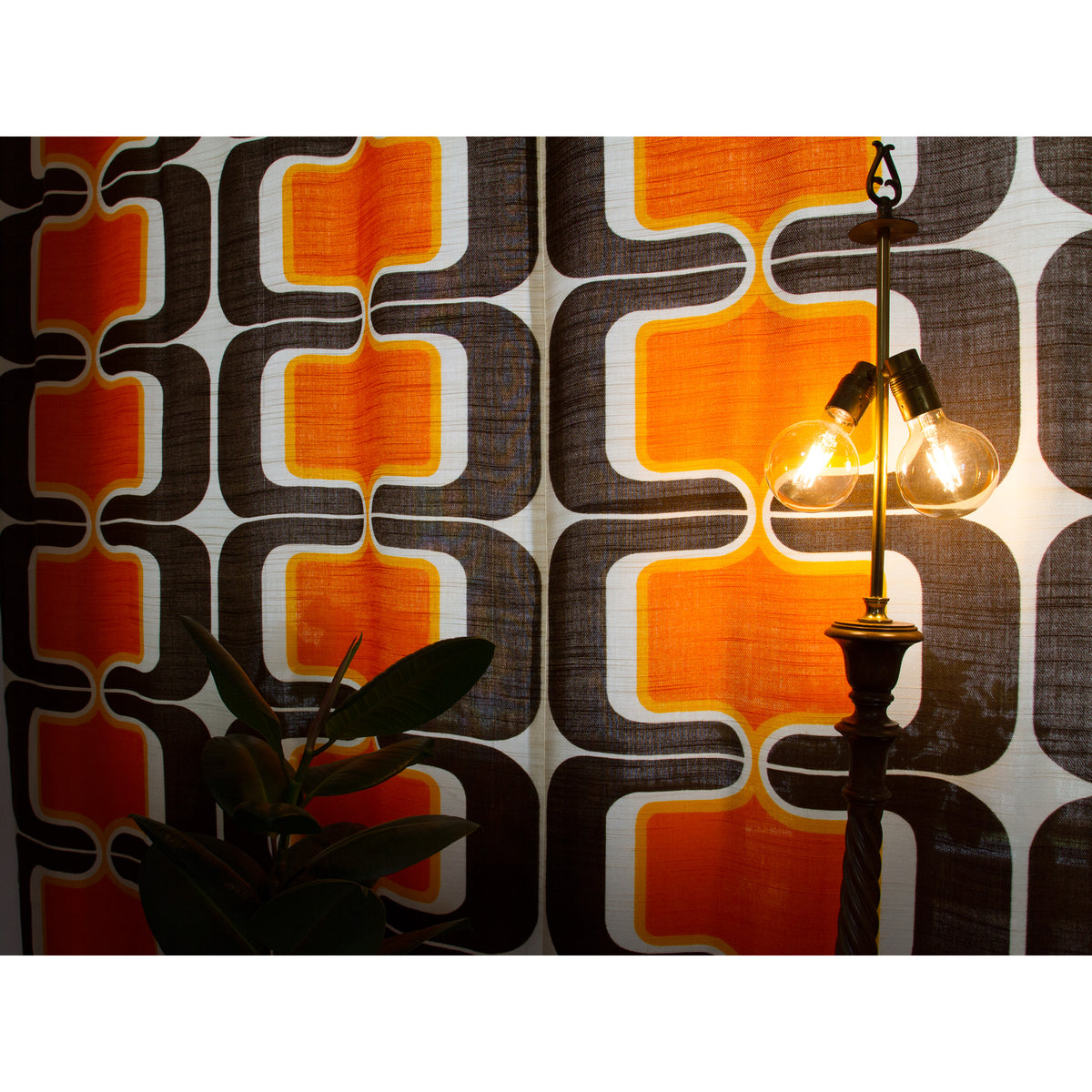Retro 60s or 70s curtain panels behind a vintage brass lamp, warm orange and brown pattern glowing in the light.