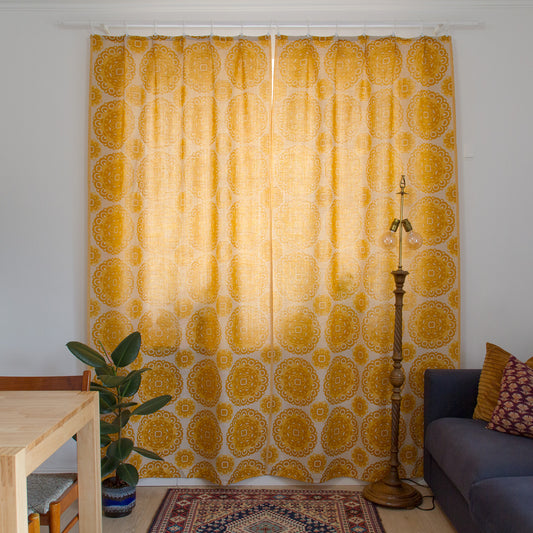 Pair of 1970s vintage curtains in mustard yellow and cream with large medallion pattern, hanging at a living room window.