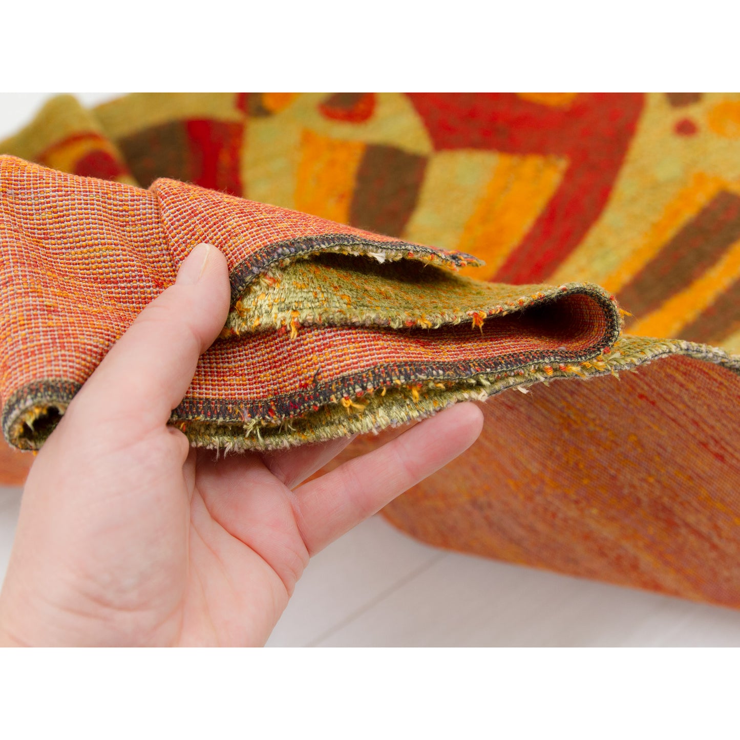 Hand holding the folded corner of the tapestry, demonstrating the pliable, soft weight and velvet-like sheen of the material.