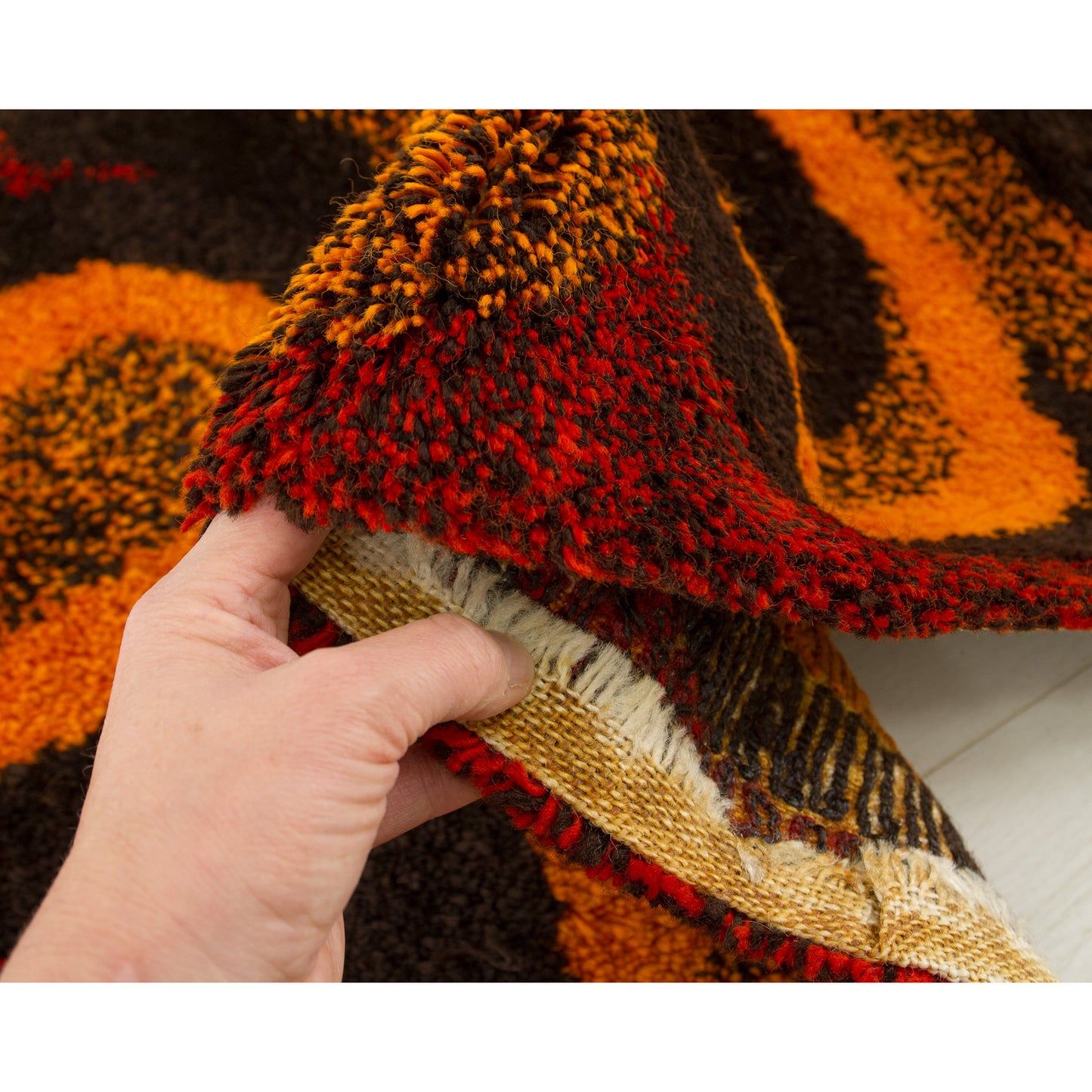 Close up checking the hem finish. The raw woven edges are securely folded back and fixed beneath, a technique ensuring the rug remains robust and durable over decades.