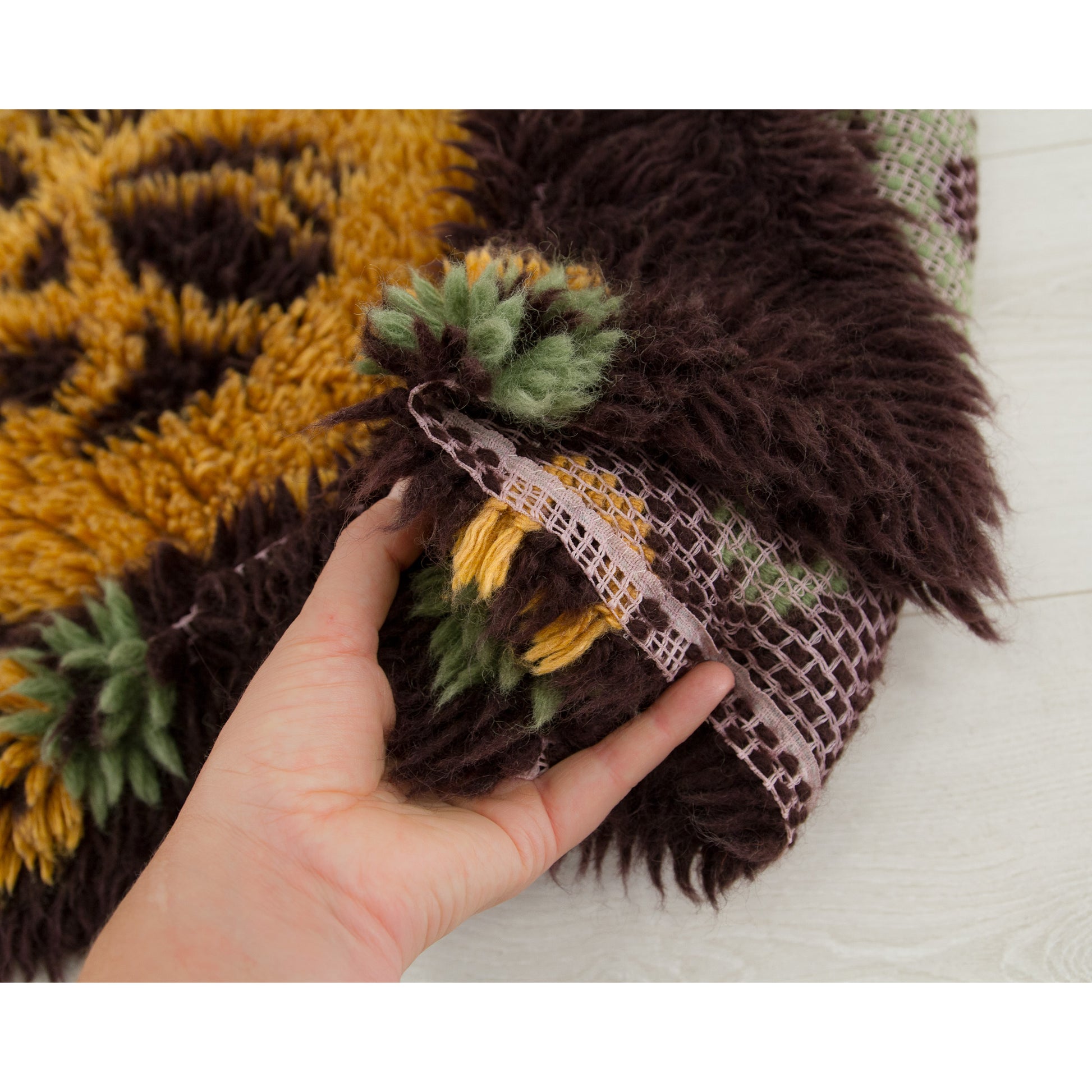 The side of the carpet gathered gracefully in a hand, permitting the viewer to marvel simultaneously at the luxurious high-pile front and the meticulously knotted canvas backing.