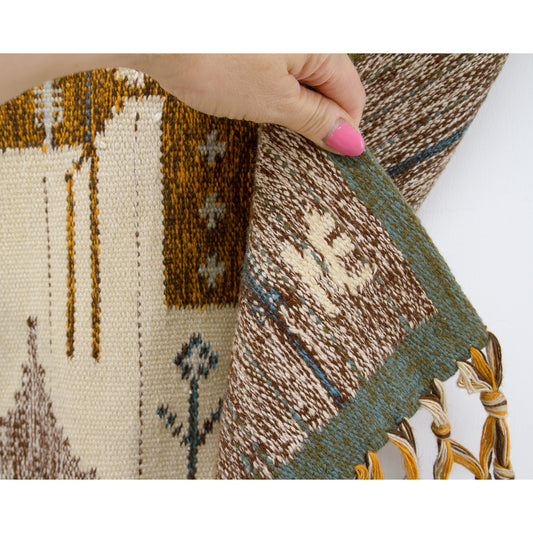 Hand holding the bottom corner of the vintage tapestry, verifying authenticity by highlighting the original artist's signature letters 'NE' proudly woven into the wool fabric.