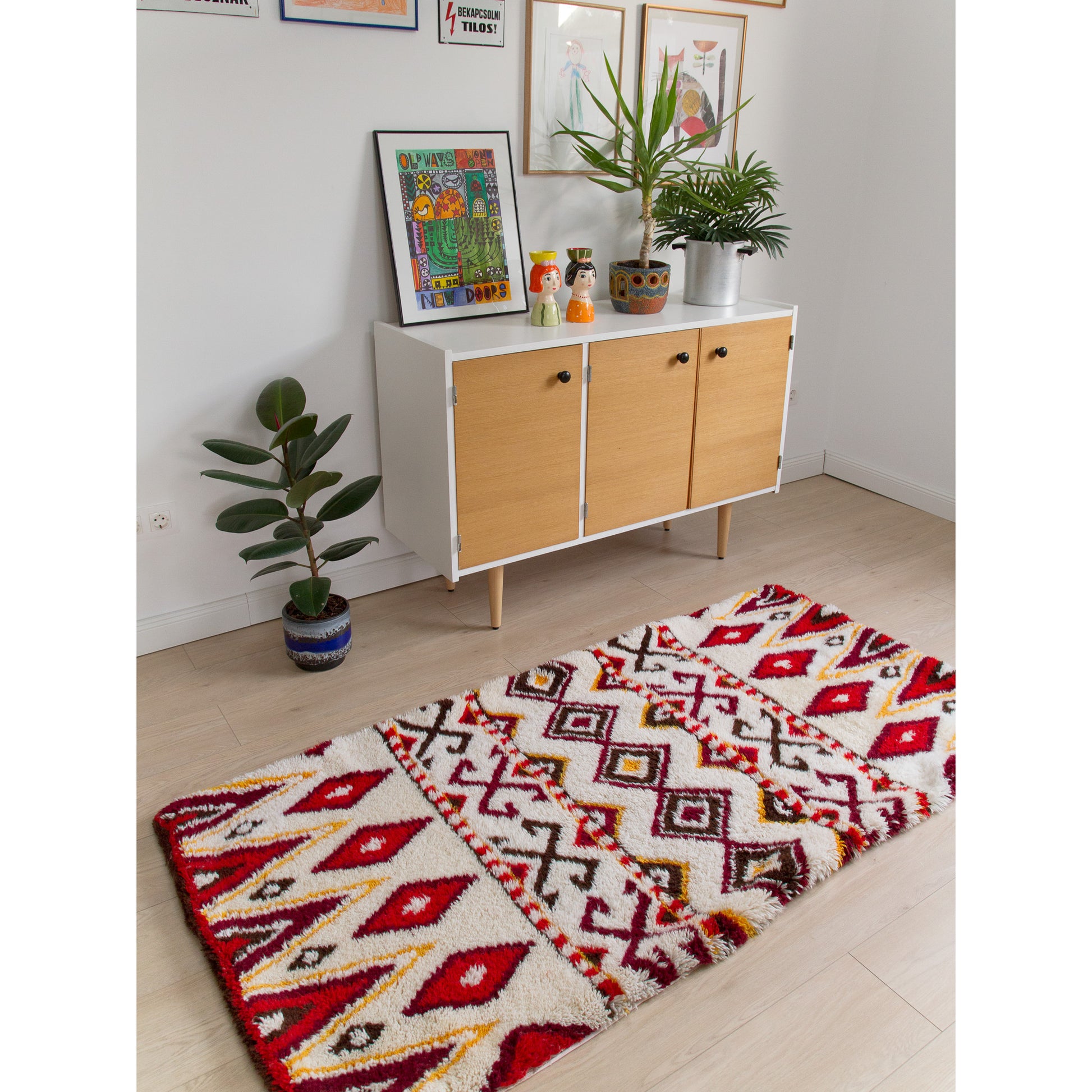 Bright red and gold tribal design vintage rug styled on a light floor in front of a mid-century modern wooden credenza, giving off incredibly cheerful boho styling vibes.