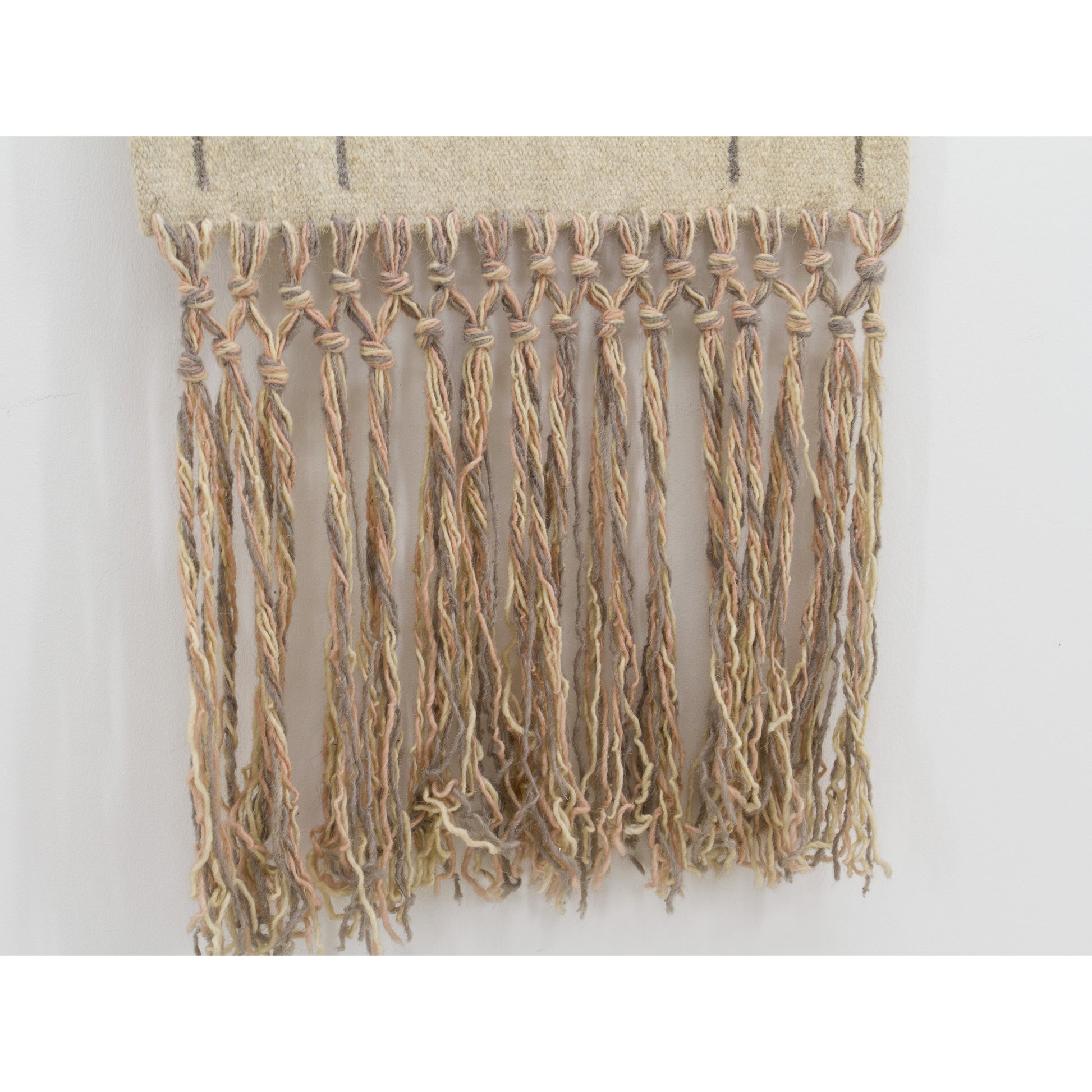 Close-up entirely focused on the sweeping 17-inch bottom fringe. Extra long, beautifully arranged macrame knots showcasing strands of cream, beige, pale pink, and grey wool yarn.