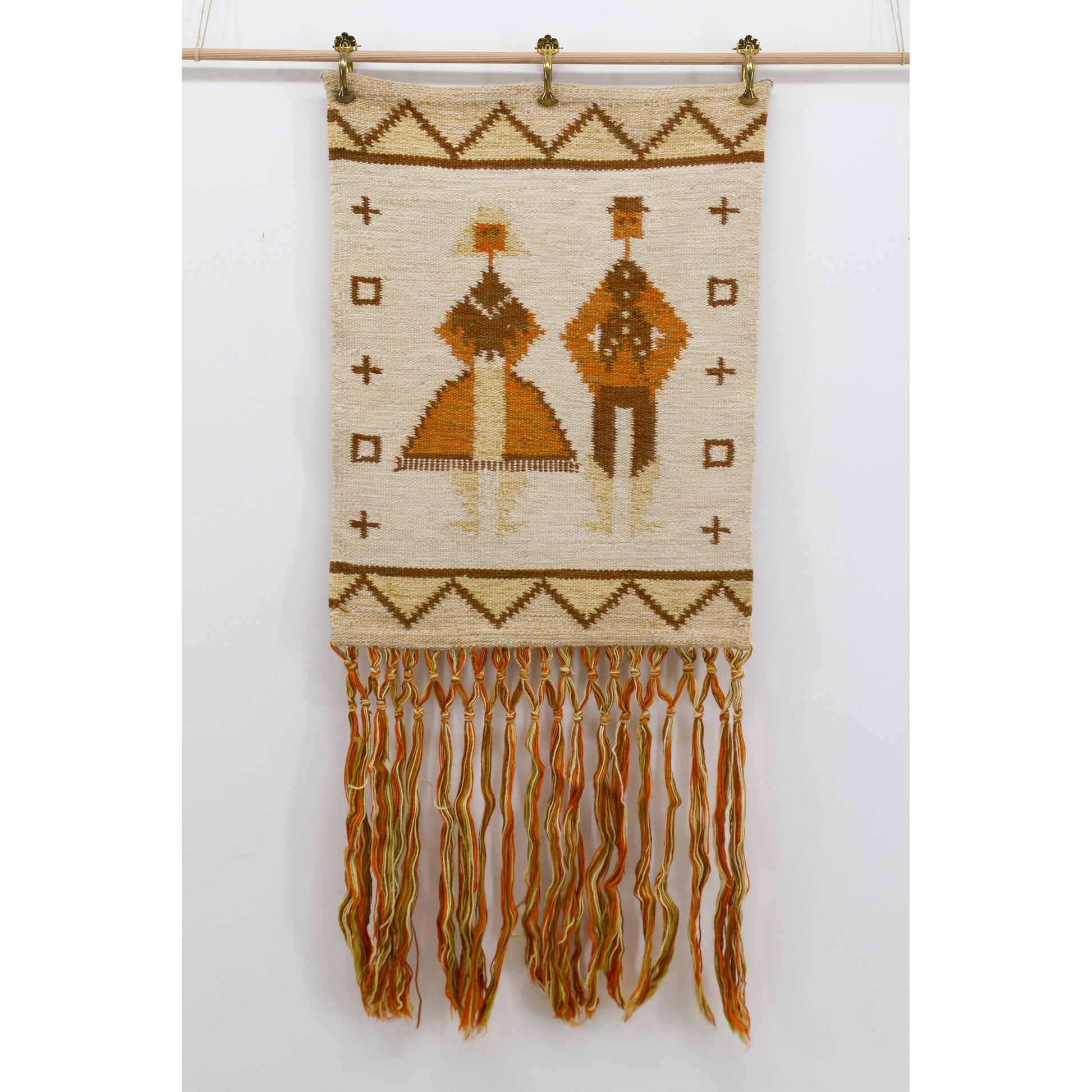 Flat view of a mid-century geometric bohemian tapestry mounted via brass clips on a wooden dowel, featuring natural wool and naive 1970s art motifs.