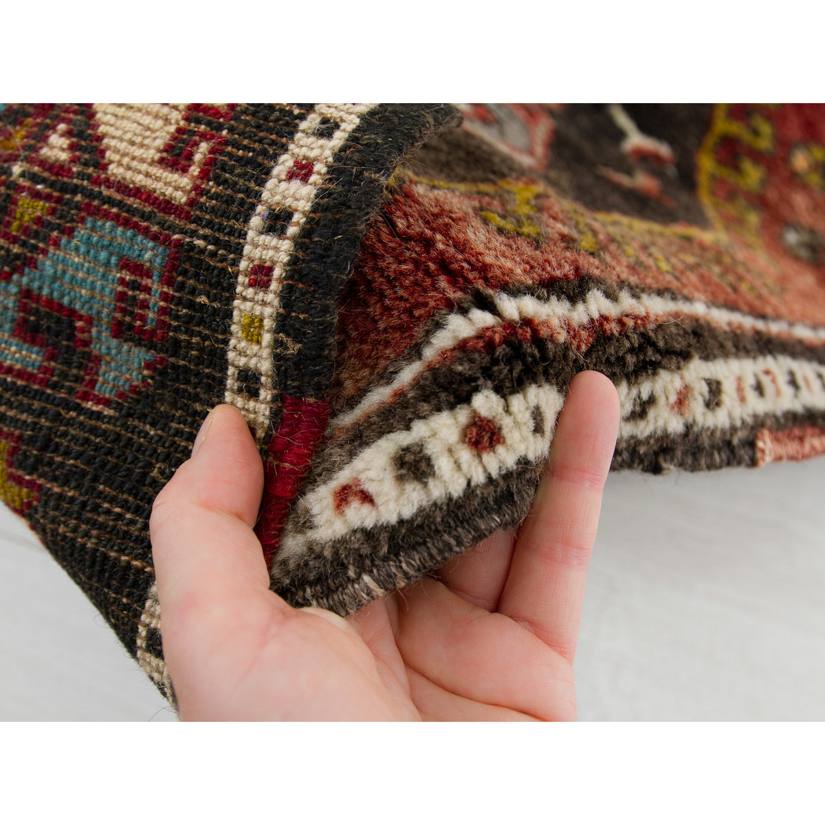 Hand bending a brown vintage Anatolian rug, showing its soft, dense hand-knotted wool pile