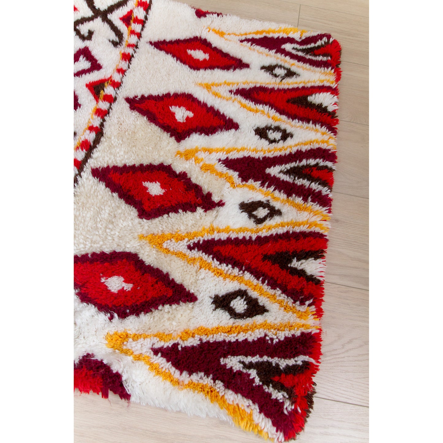 View focusing on the shorter border edge of the vintage shag runner. Rich repeating tribal diamond motifs in brilliant warm red, gold, brown, and pure white.