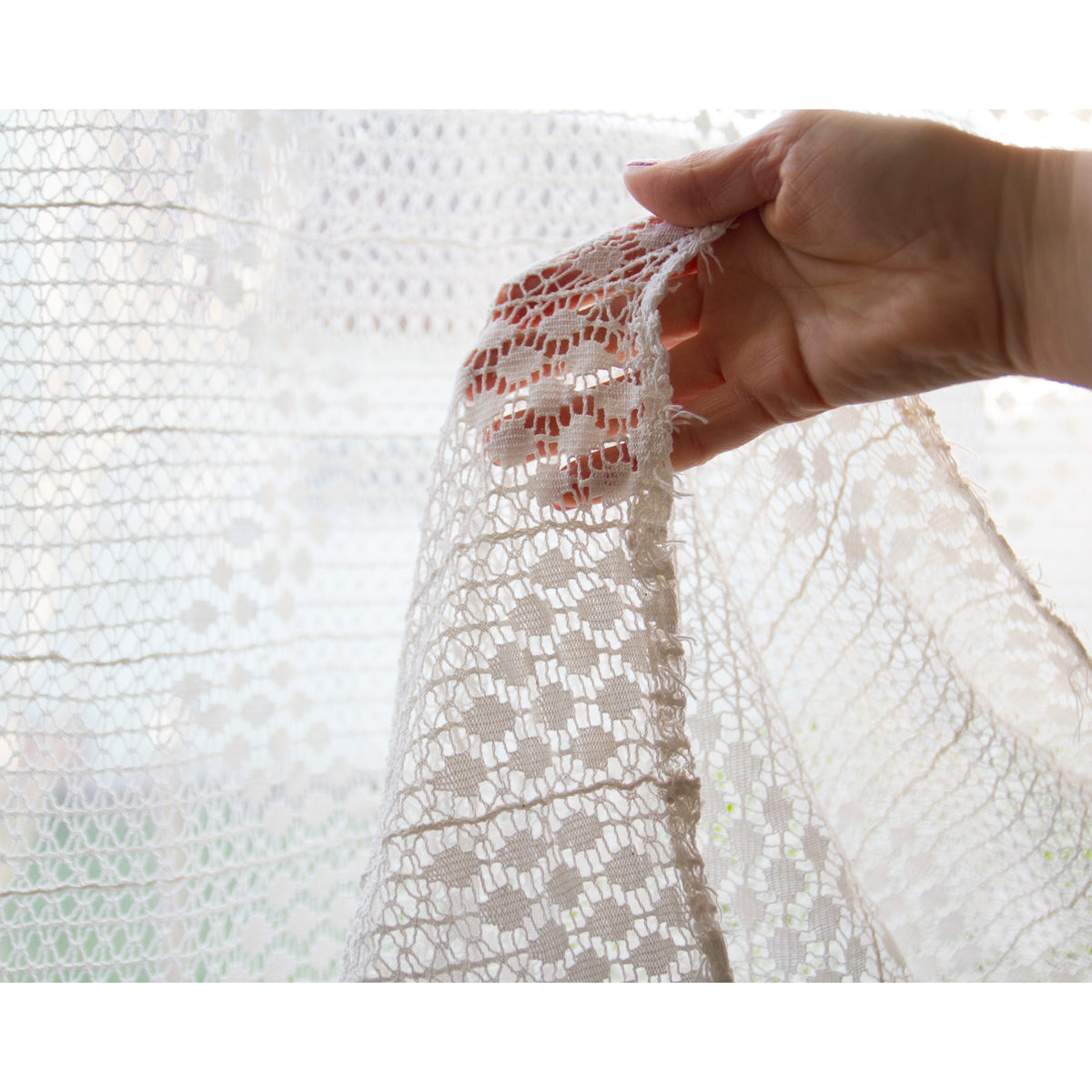 Delicate white lace fabric held up to the window, perfect for sewing, crafts or wedding decor