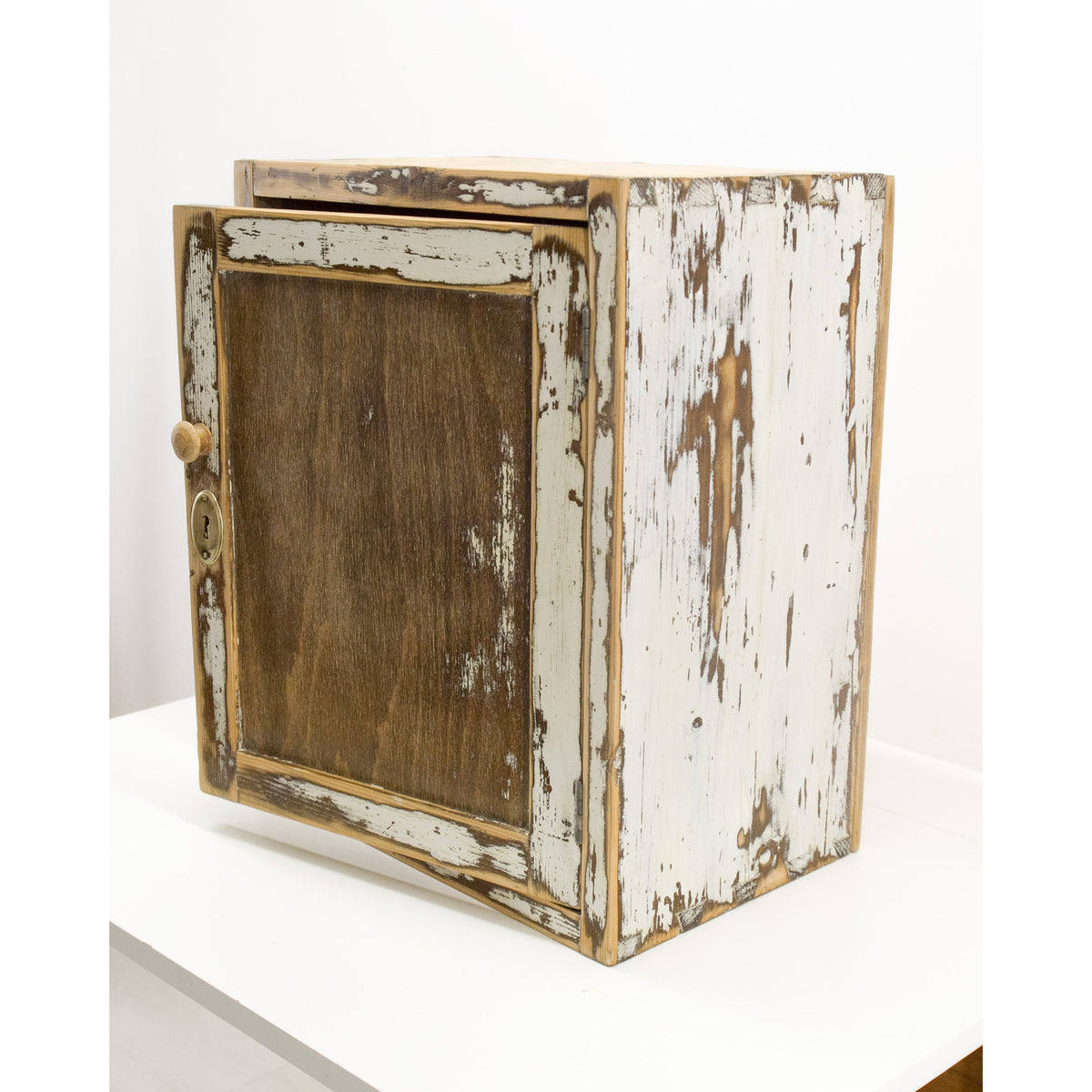 Side view of the vintage rustic wooden cabinet with a distressed white paint finish, featuring a dark brown wood door panel and a small round knob, displayed on a white surface against a white background. The furniture has a strong antique-rustic vibe that makes it perfect for a shaker or farmhouse style kitchen or bathroom.