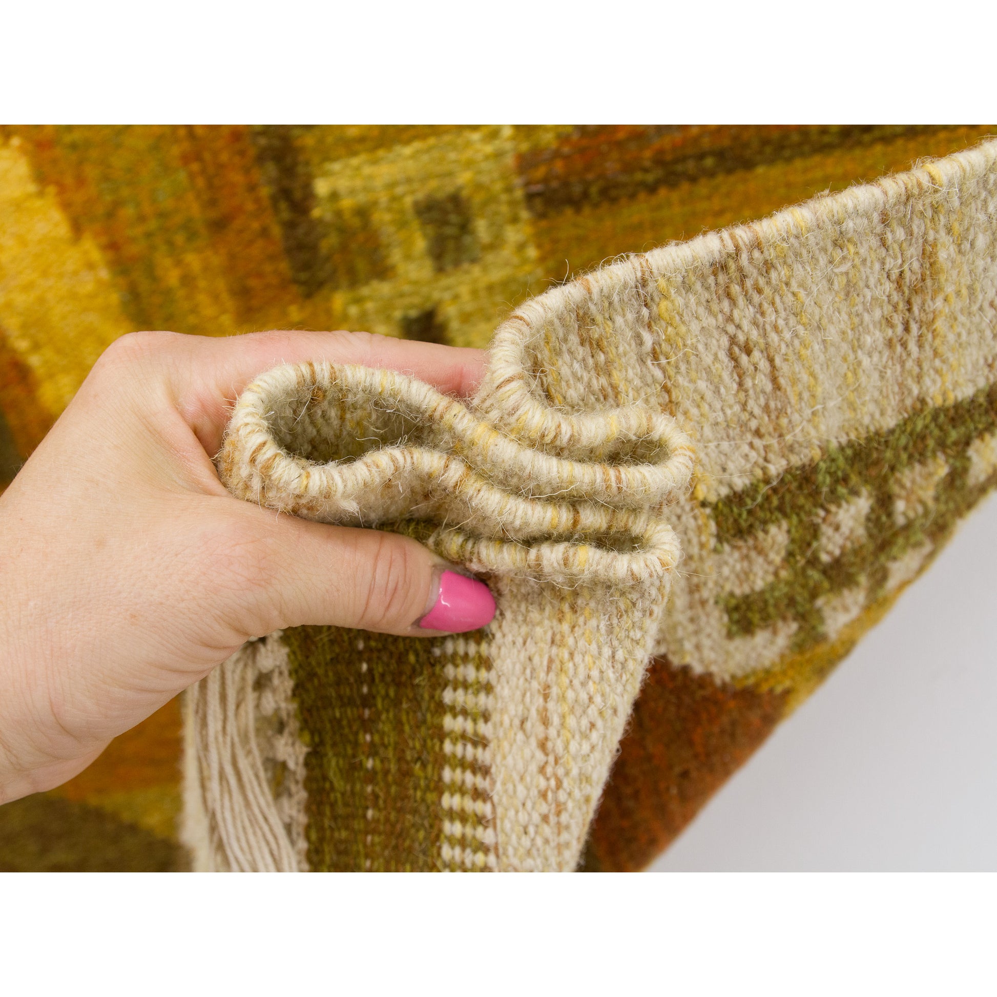 Hand grasping and gathering the sturdy flatweave edge of the rug to showcase the high quality, soft, yet heavy-duty traditional Hungarian weaving material.