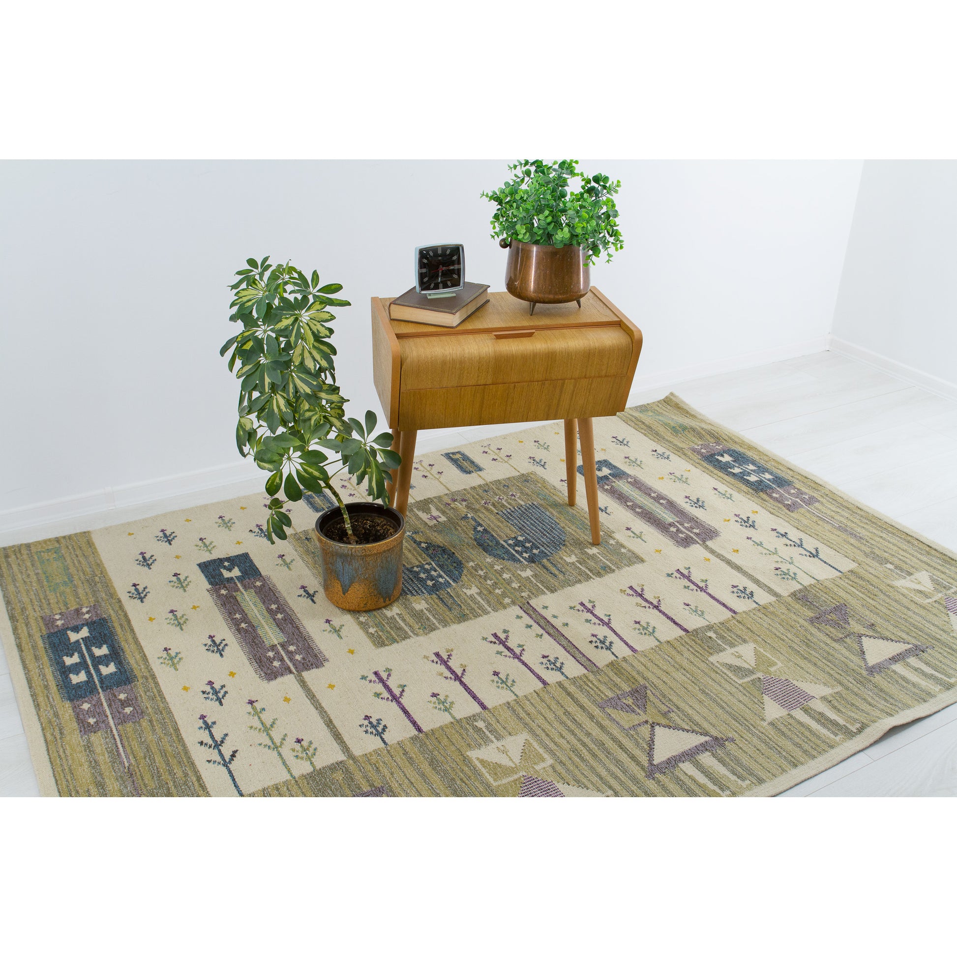 Extra large Eva Nemeth handwoven rug styled elegantly on the floor under a classic 1960s oak side table with a green houseplant.