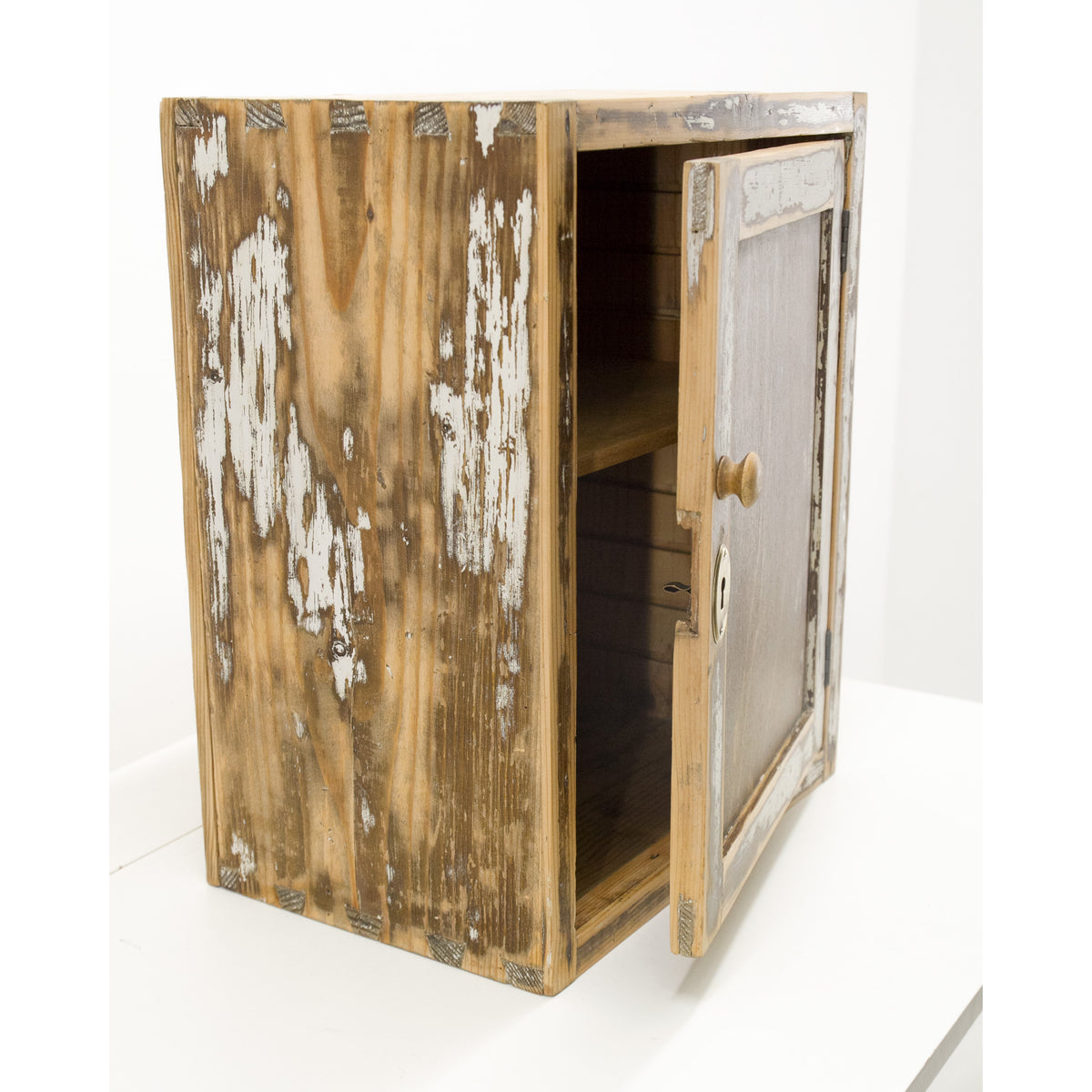 French country style bathroom cabinet with a distressed finish, featuring peeling white paint over a brown wood grain, with the door swung open to reveal shelves inside. Expertly refurbished antique furniture for a rustic, provance or french country style home.