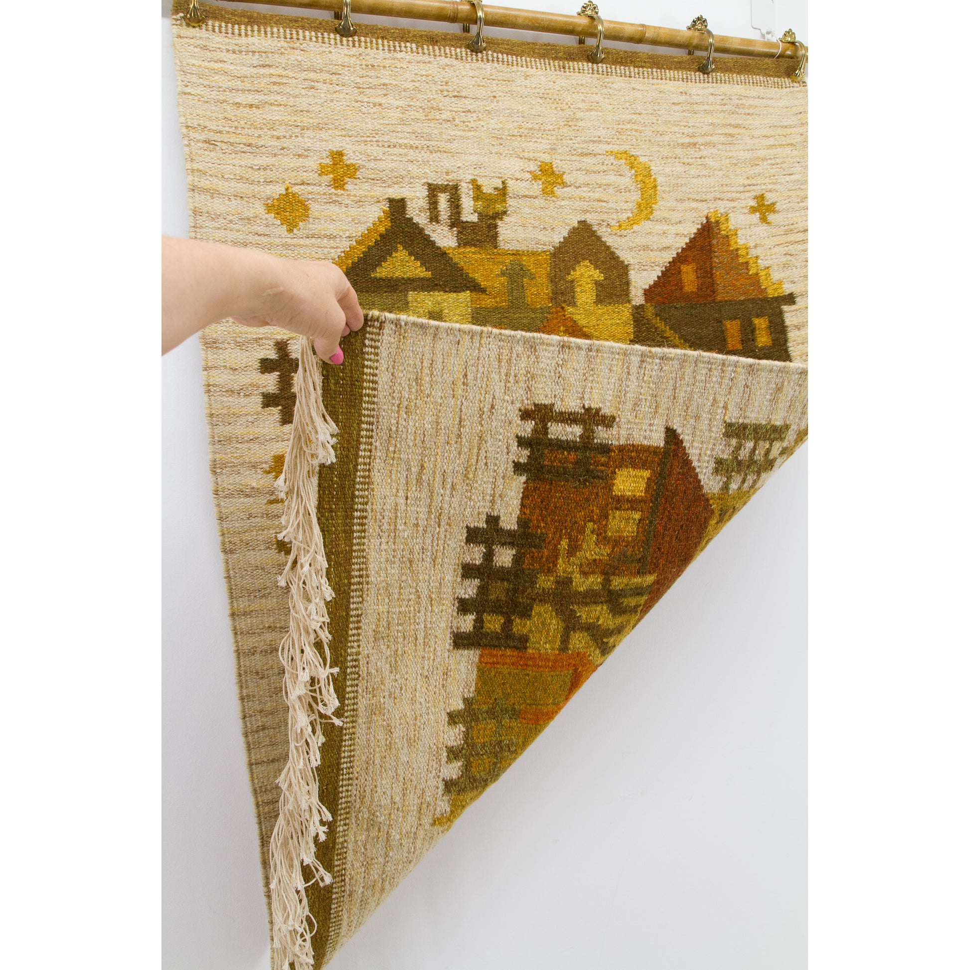 Hand peeling back one heavy corner of the hanging art, providing visual proof that the intricate retro colors mirror perfectly onto the fully reversible back.