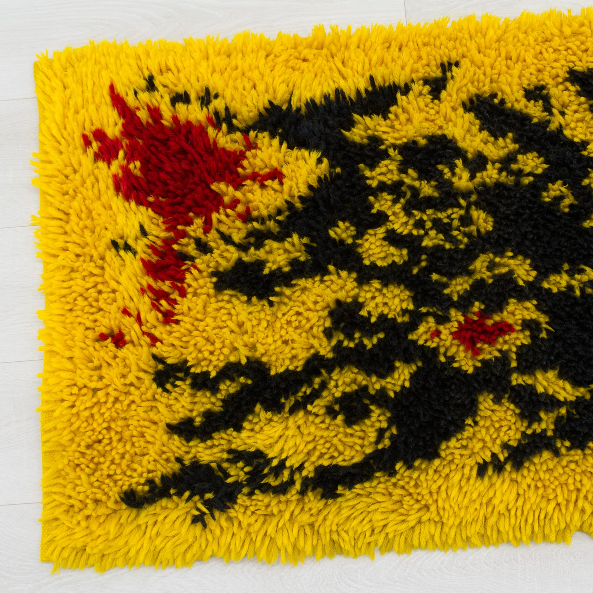Close-up of the thick, fluffy piles of the vintage rug. The high pile shag texture contrasts deep black and bright yellow in this 1970s mid century tapestry.