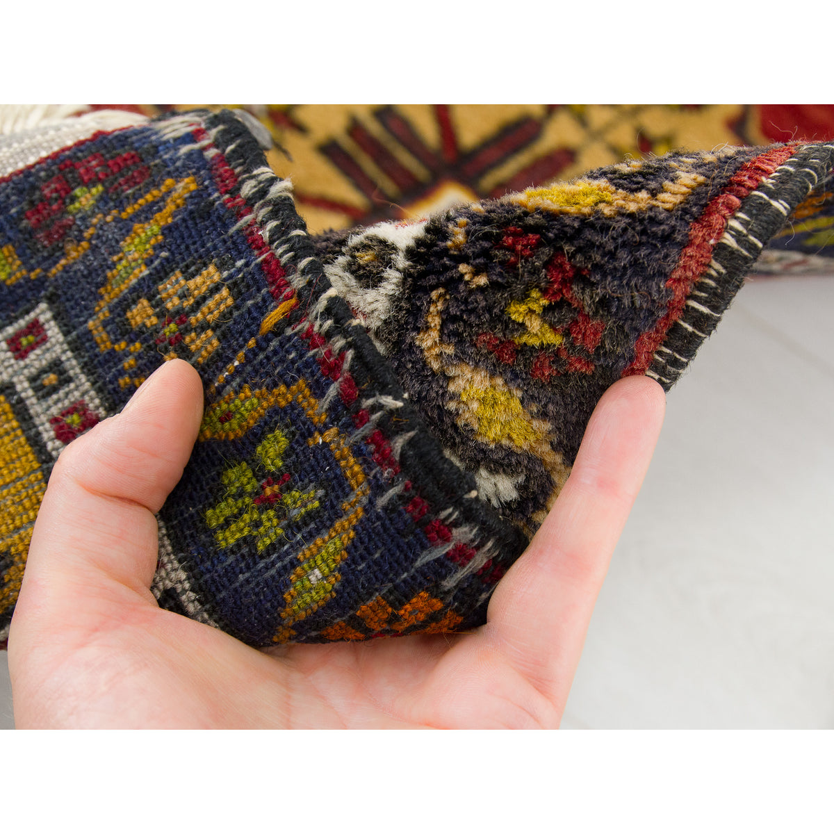 Hand folding a small vintage navy and red rug to show the thickness of the wool pile