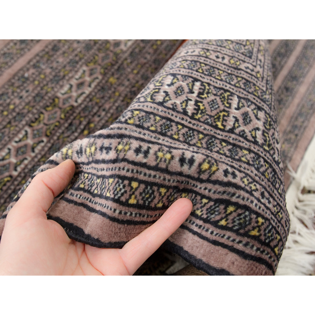 Hand holding the edge of a hand-knotted rug, close-up of the detailed tribal border and fine, dense silk piles