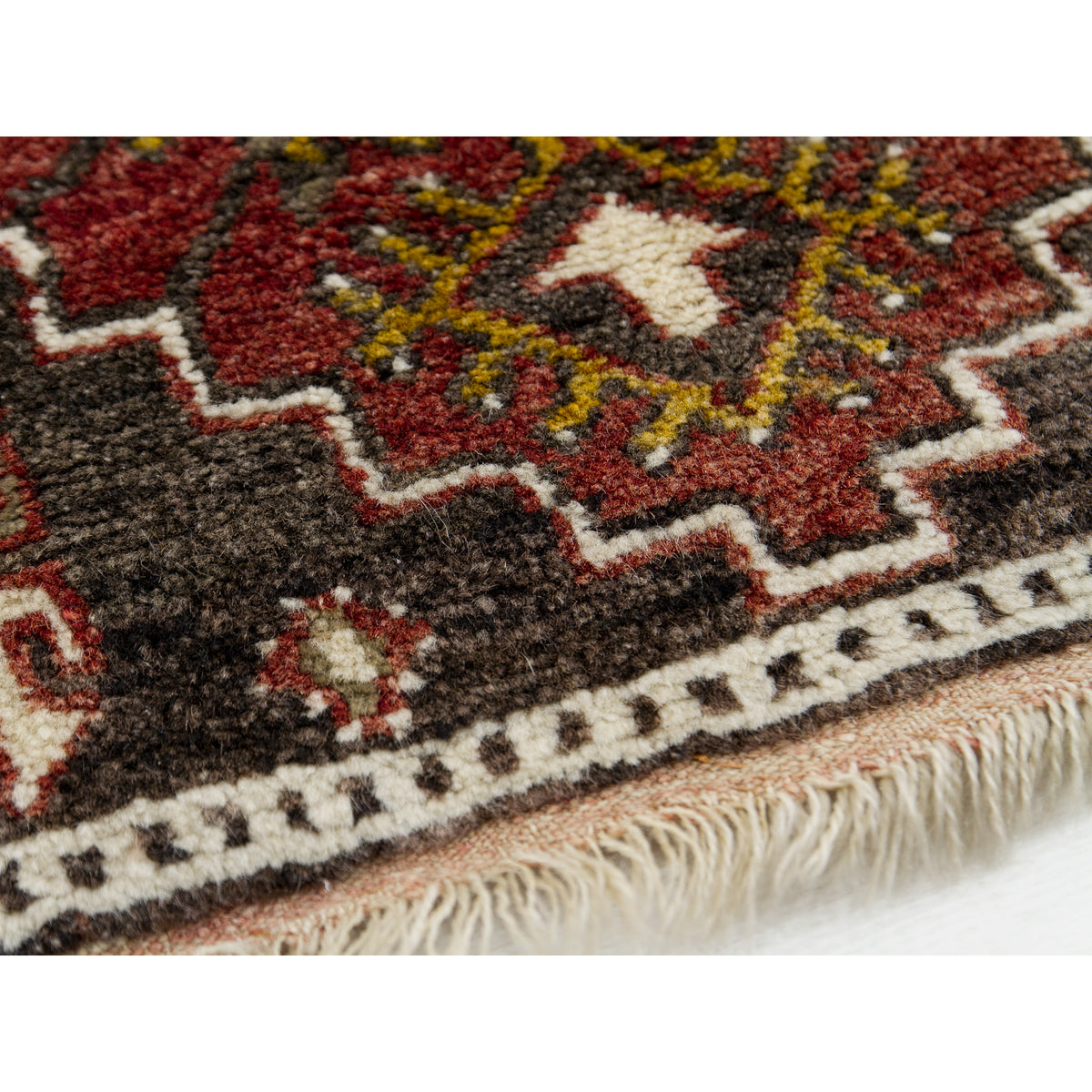 Close-up of a hand-knotted brown wool rug with a stepped red medallion, ivory border and fringe