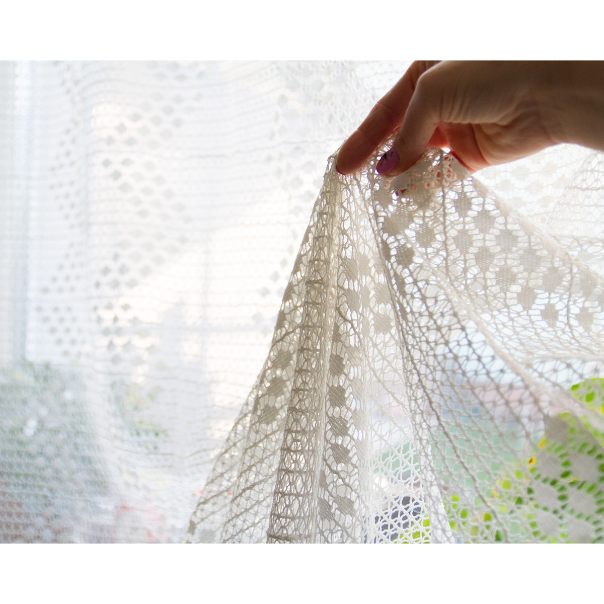 Hand lifting the edge of a vintage lace curtain against the light, showing the delicate openwork