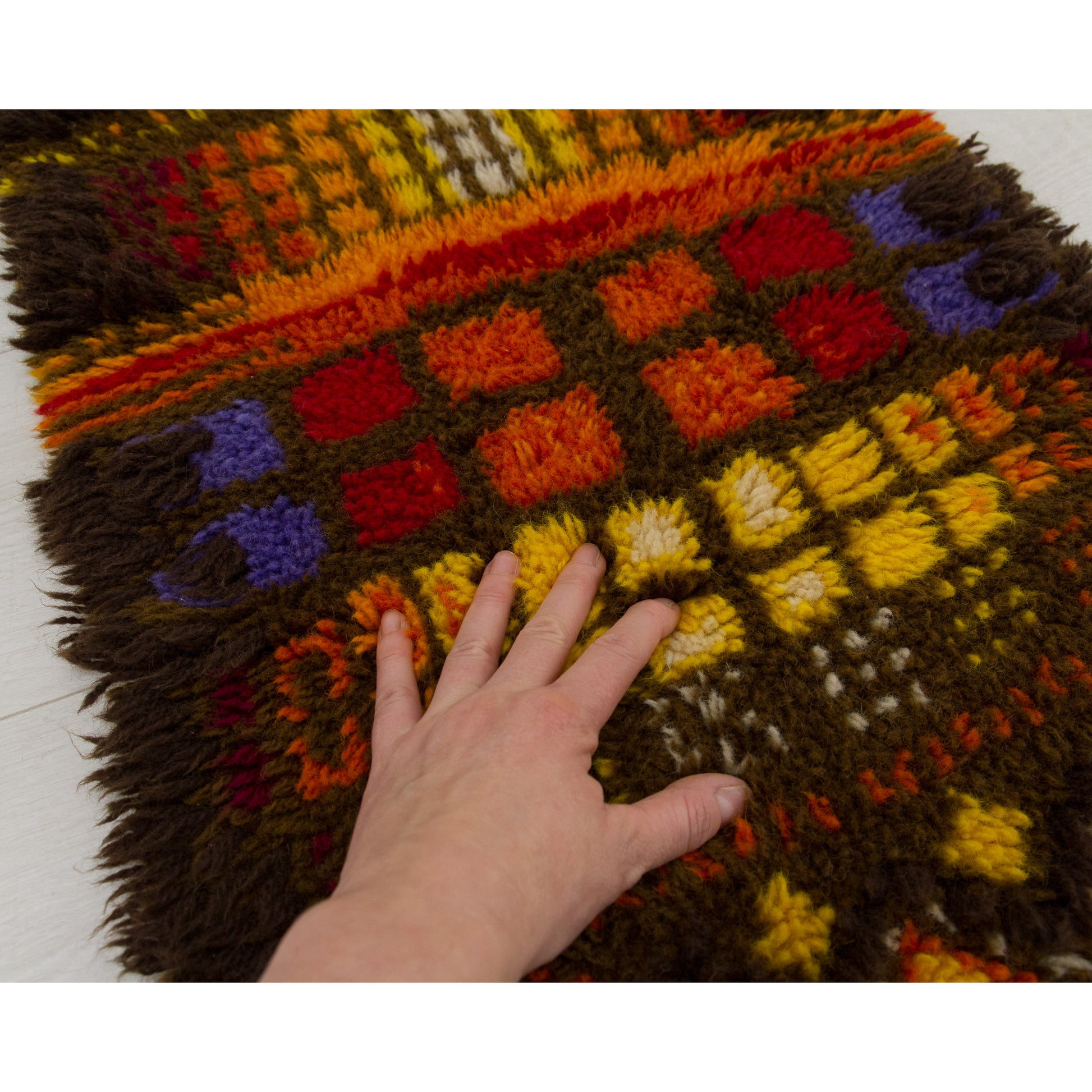 A hand gently touching the surface of the colorful 1970s rya rug to demonstrate the soft, incredibly cozy and plush cotton yarn texture.