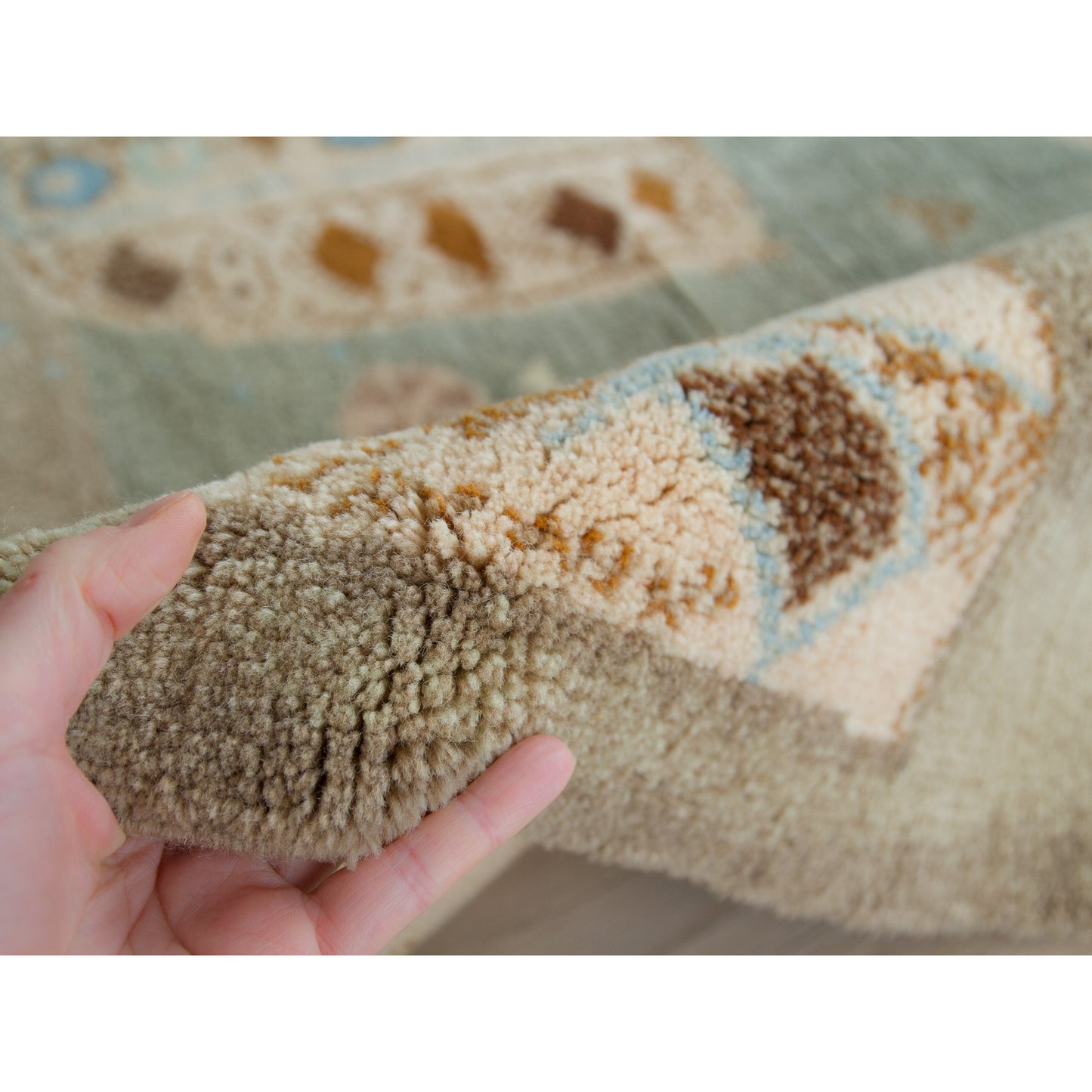 Hand holding the edge of the tapestry. The deep, super fine wool piles of the vintage rug show the tactile warmth and exquisite high quality of this mid century tapestry.