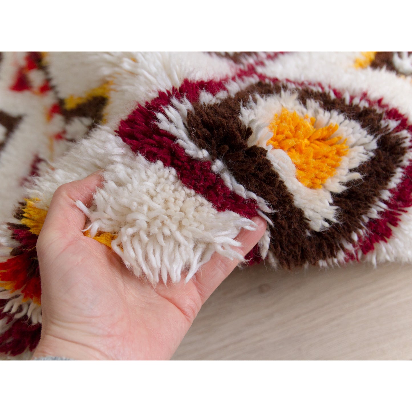 Hand holding the thick, plush woven edge of the handmade geometric shag throw, showing how dense, durable, and exceptionally soft the cotton piles are.