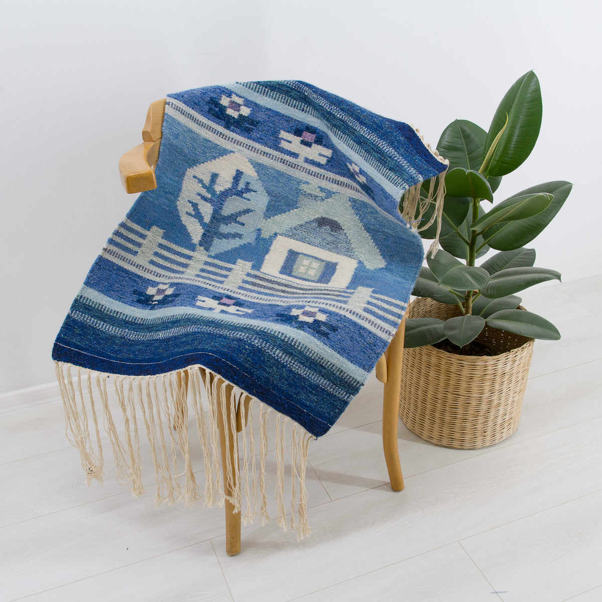 The tapestry draped over a dining chair to demonstrate scale and showcasing the long fringe on the ends. Blue and cream woven pattern perfect for cottagecore dining decor.
