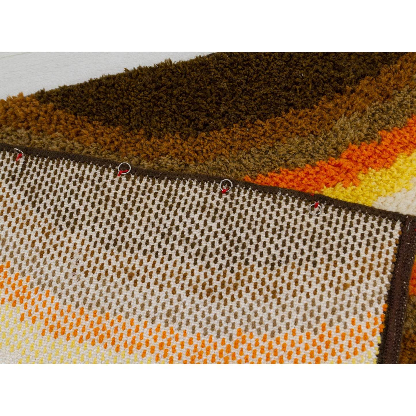 Hanging mechanism featuring discrete rings attached to the back of the vintage rya rug.