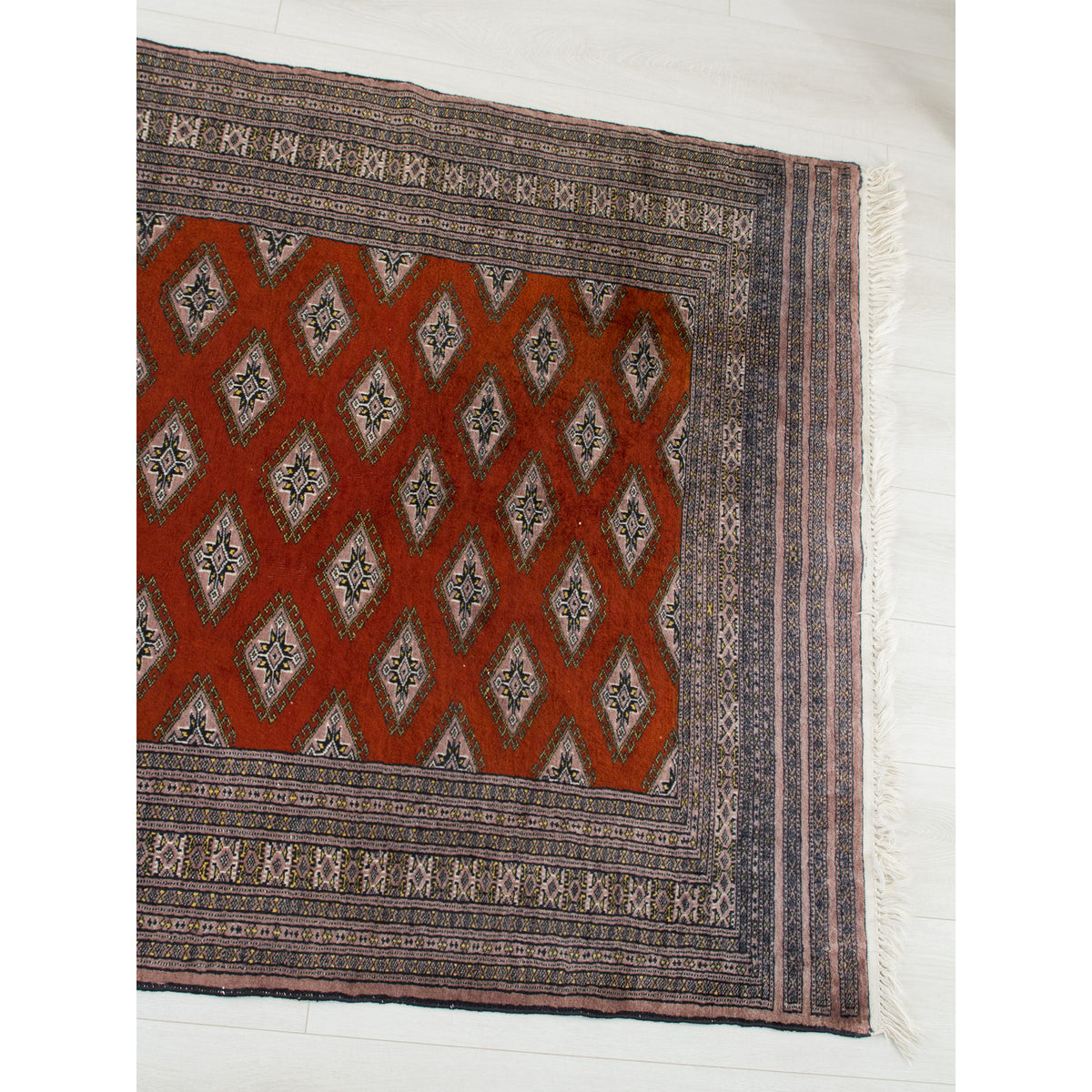 Top view of Jaldar style rug with rust red field and wide mauve tribal borders